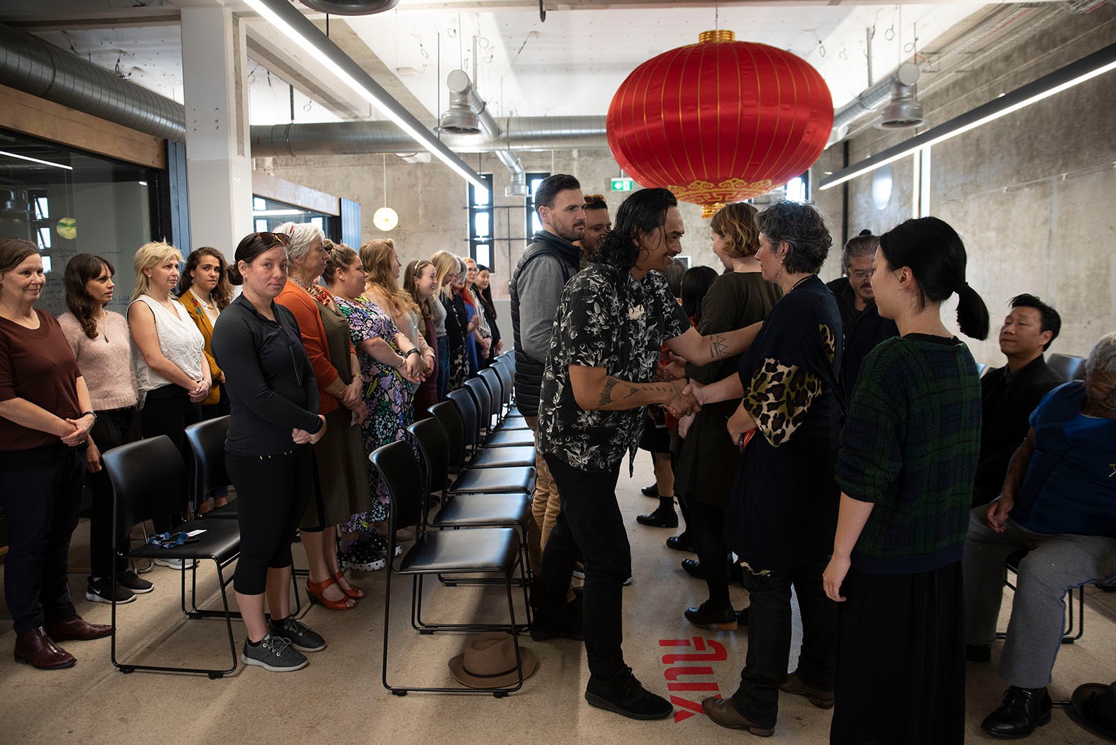 The front rows of a pōwhiri shake hands and hongi, as other rows wait.