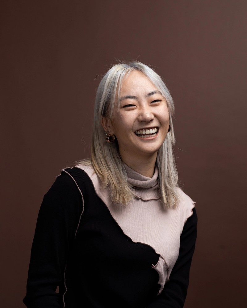 Nahyeon has mid-length silver hair and is laughing for the camera in front of a dark background.