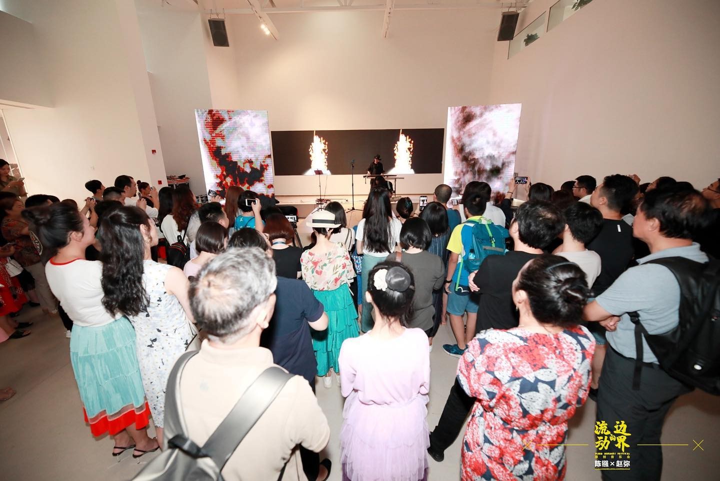 Wide shot of the live performance, with the artist playing handmade instrument on the stage surrounded by lots of audiences