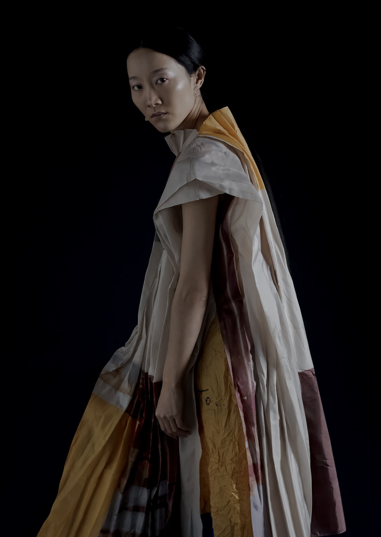 full body shot of an asian woman wearing draped materials in muted yellow, mlberry and oat