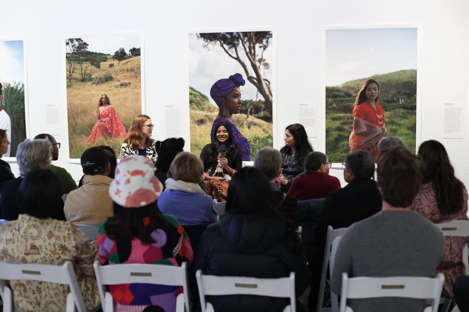 Three people speaking to a group of audience members in front of photographic portraits