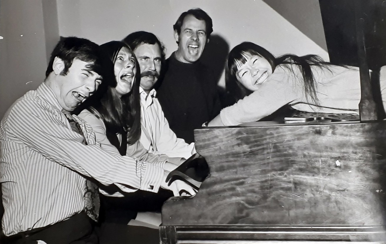 Helene Wong lies on a piano while the other actors pull faces and pretend to play.