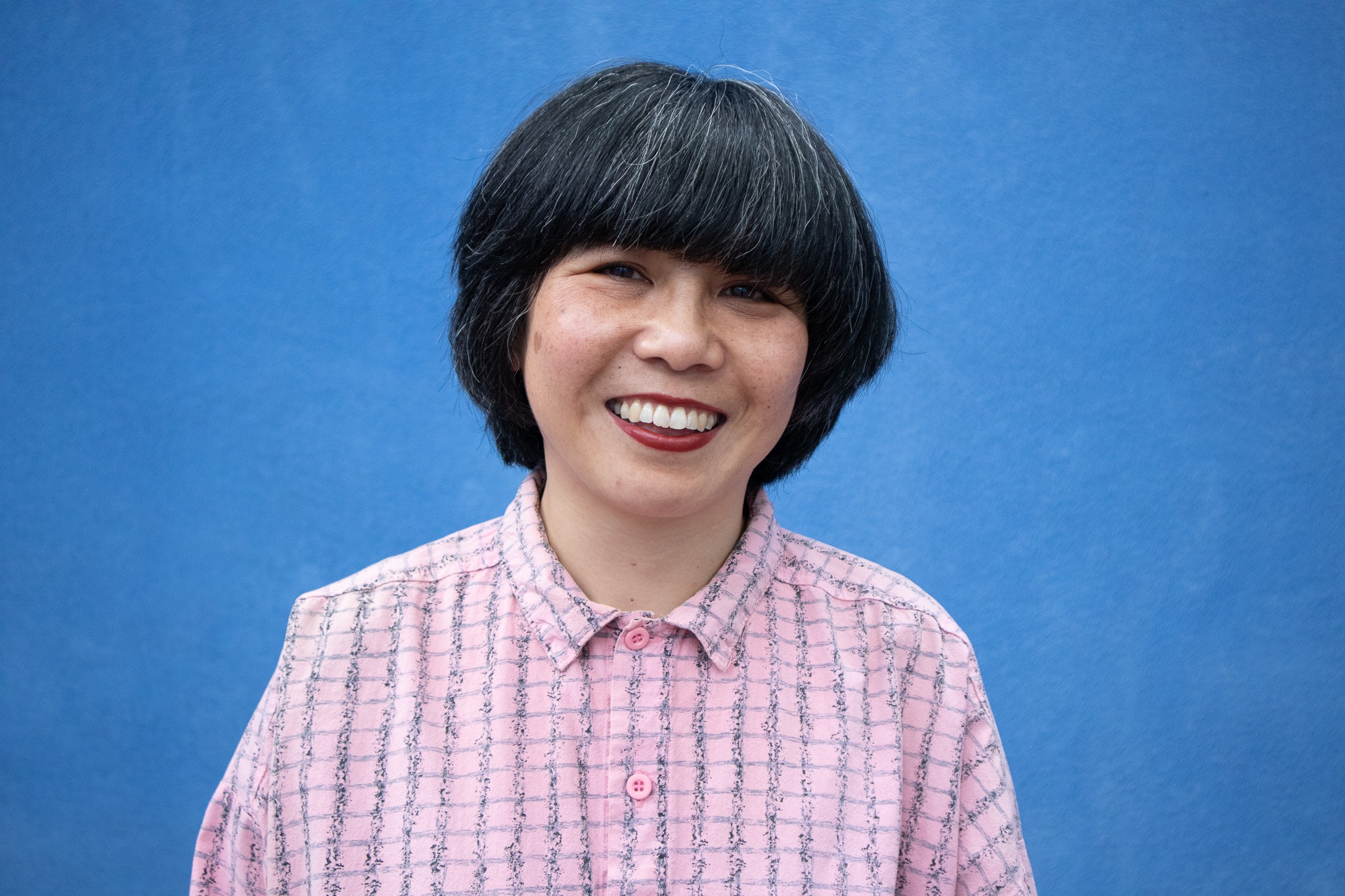 A smiling woman with a black bob and pink shirt against a blue background