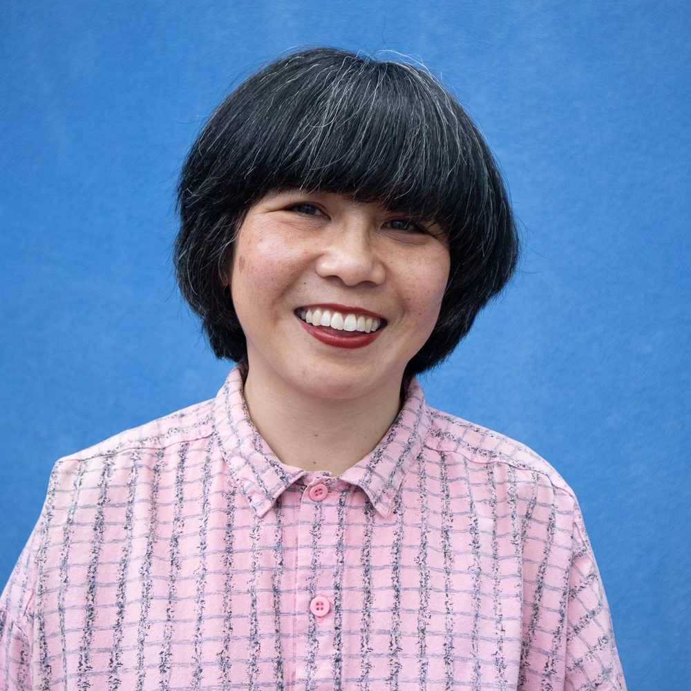 A smiling woman with a black bob and pink shirt against a blue background