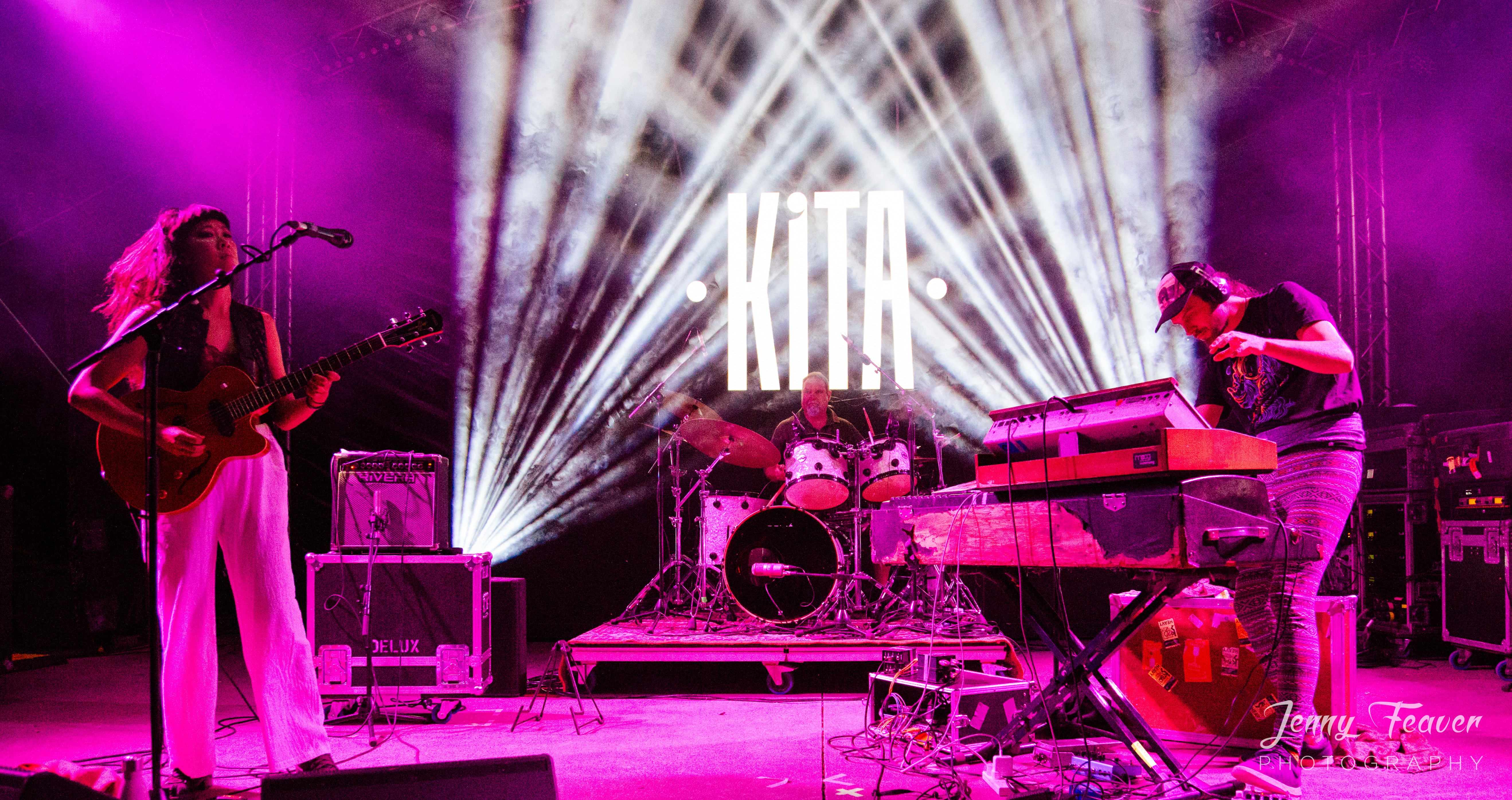 Pink lit three-piece band performing on stage