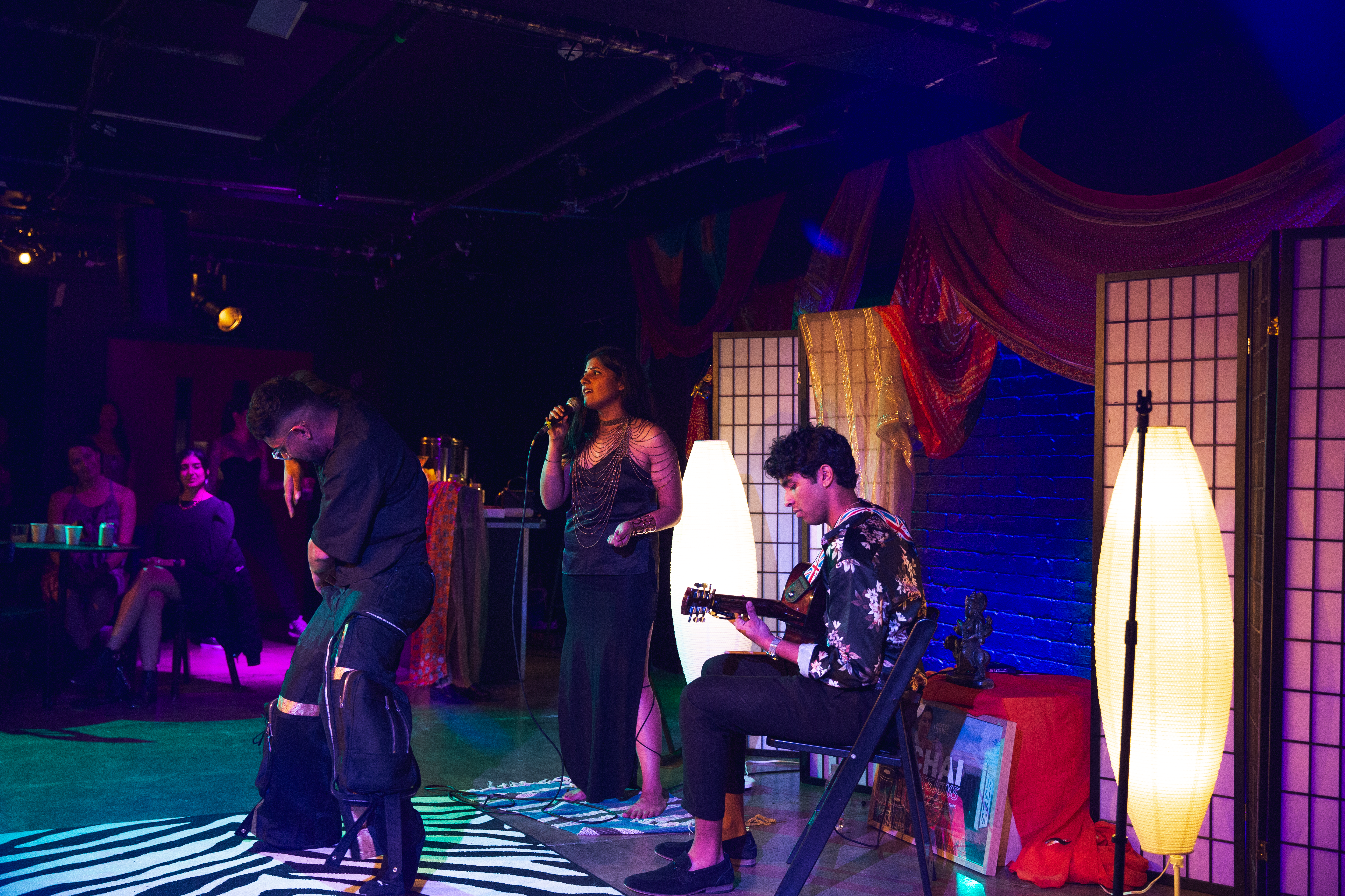 A dancer, singer, and guitarist performing on stage in a multicoloured-lit room