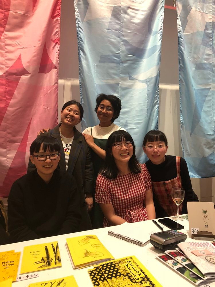 A group of people smiling together with various zines presented in front.