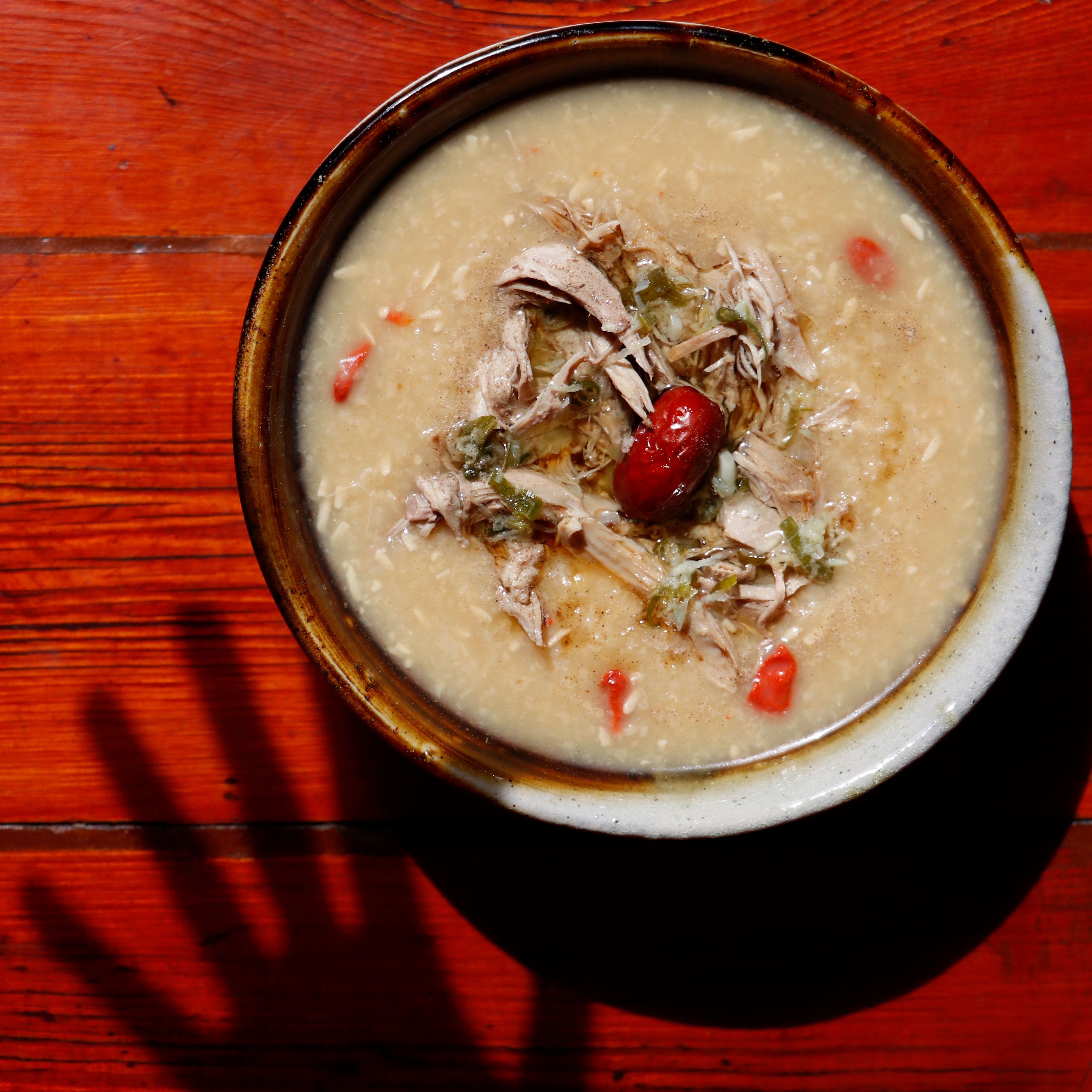 A bowl of congee on a red table with the shadow of a hand above it.