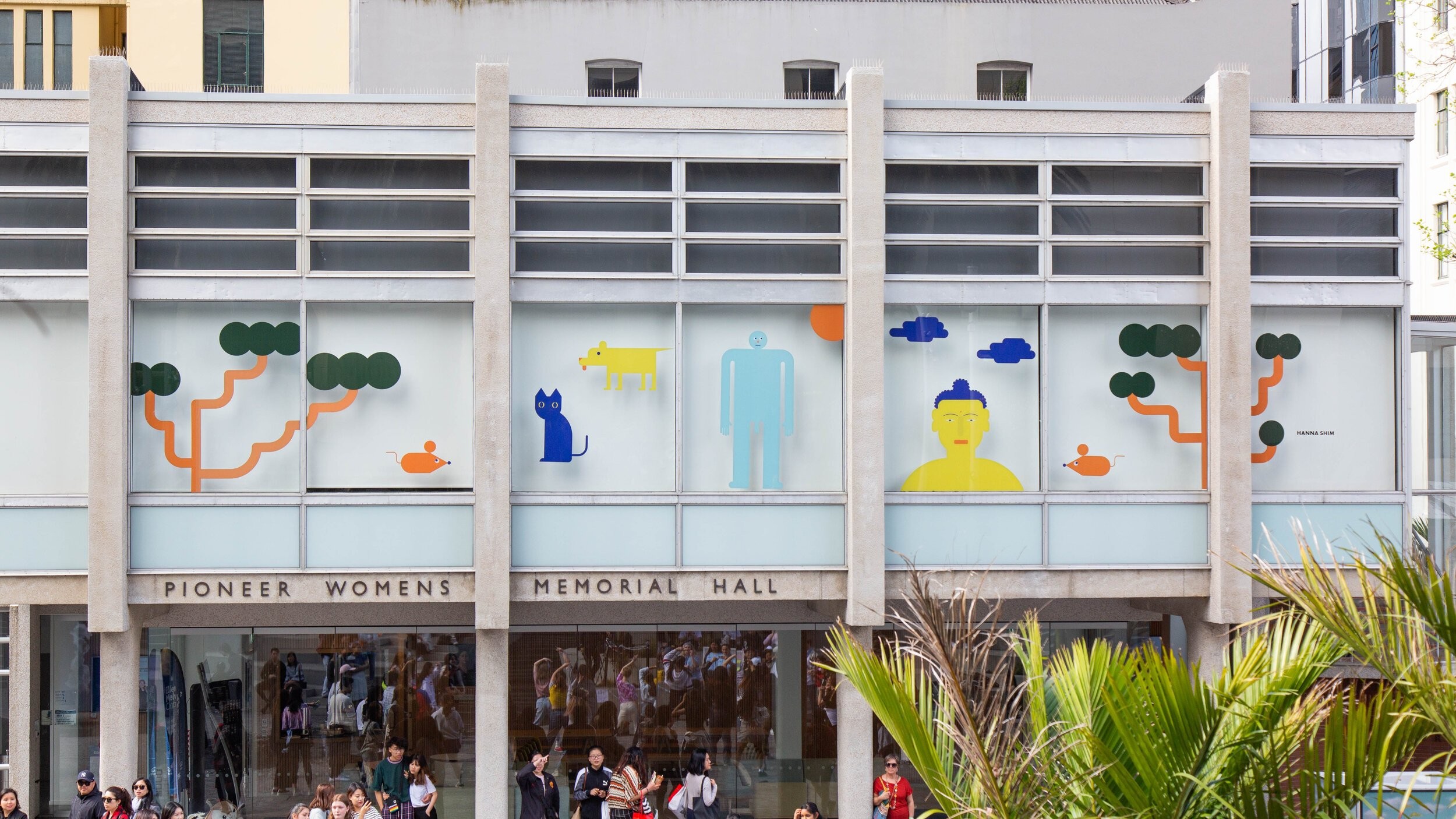 A shot of a glass window with colourful decals of trees, a cat, a mouse, and some people