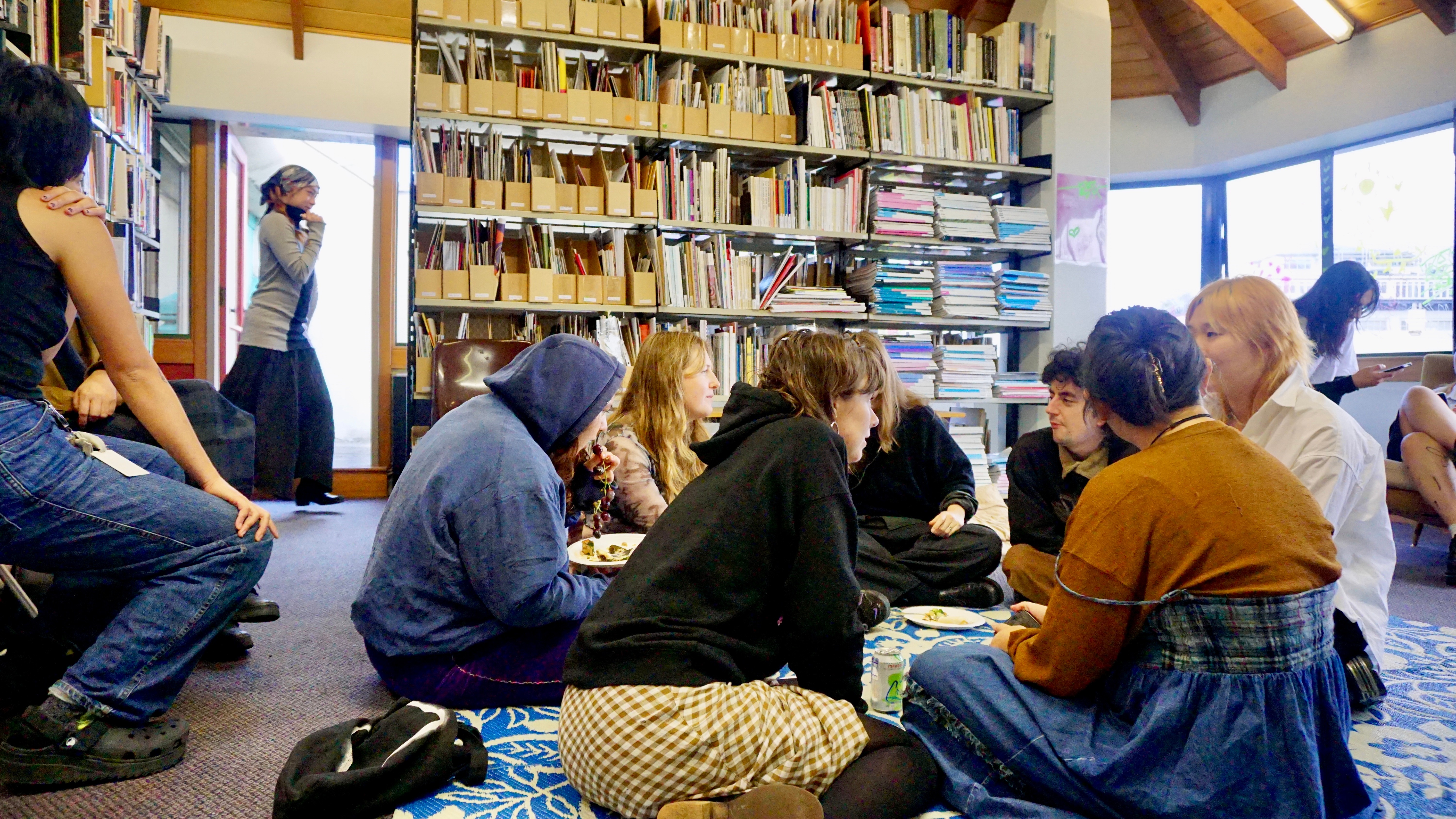 People sitting in circle on the ground, chatting in a library