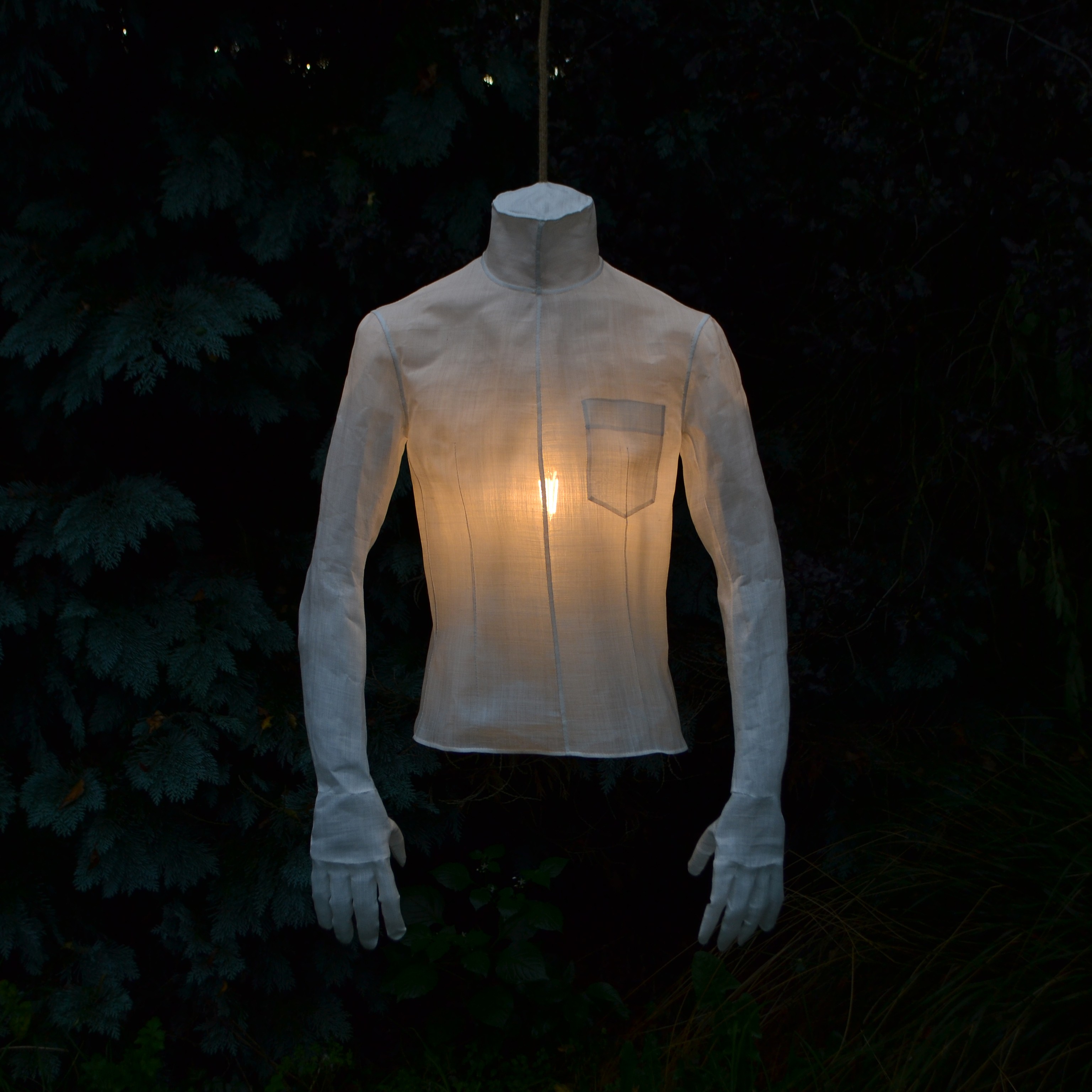 A shirt complete with fingers at the end of the arms, hanging illuminated by a light inside.