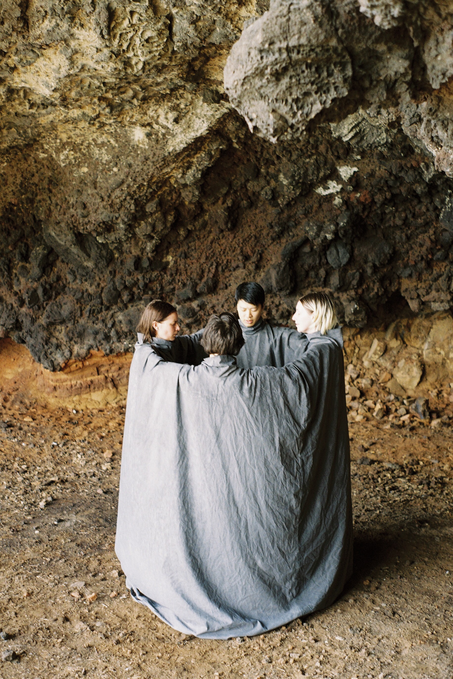 Four people in a conjoined costume huddle beneath a rock formation.