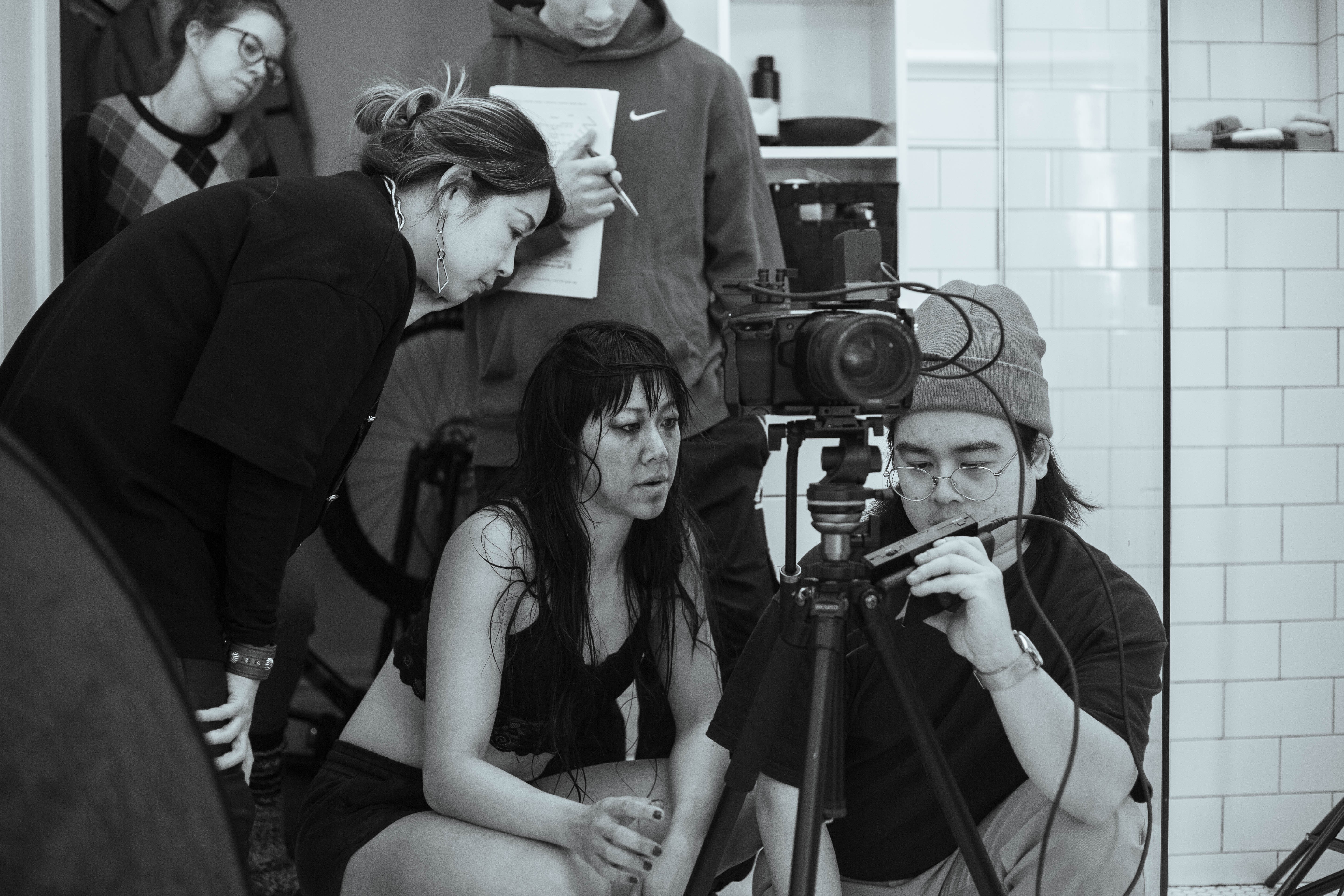 A woman with wet hair surrounded by a film crew watching footage