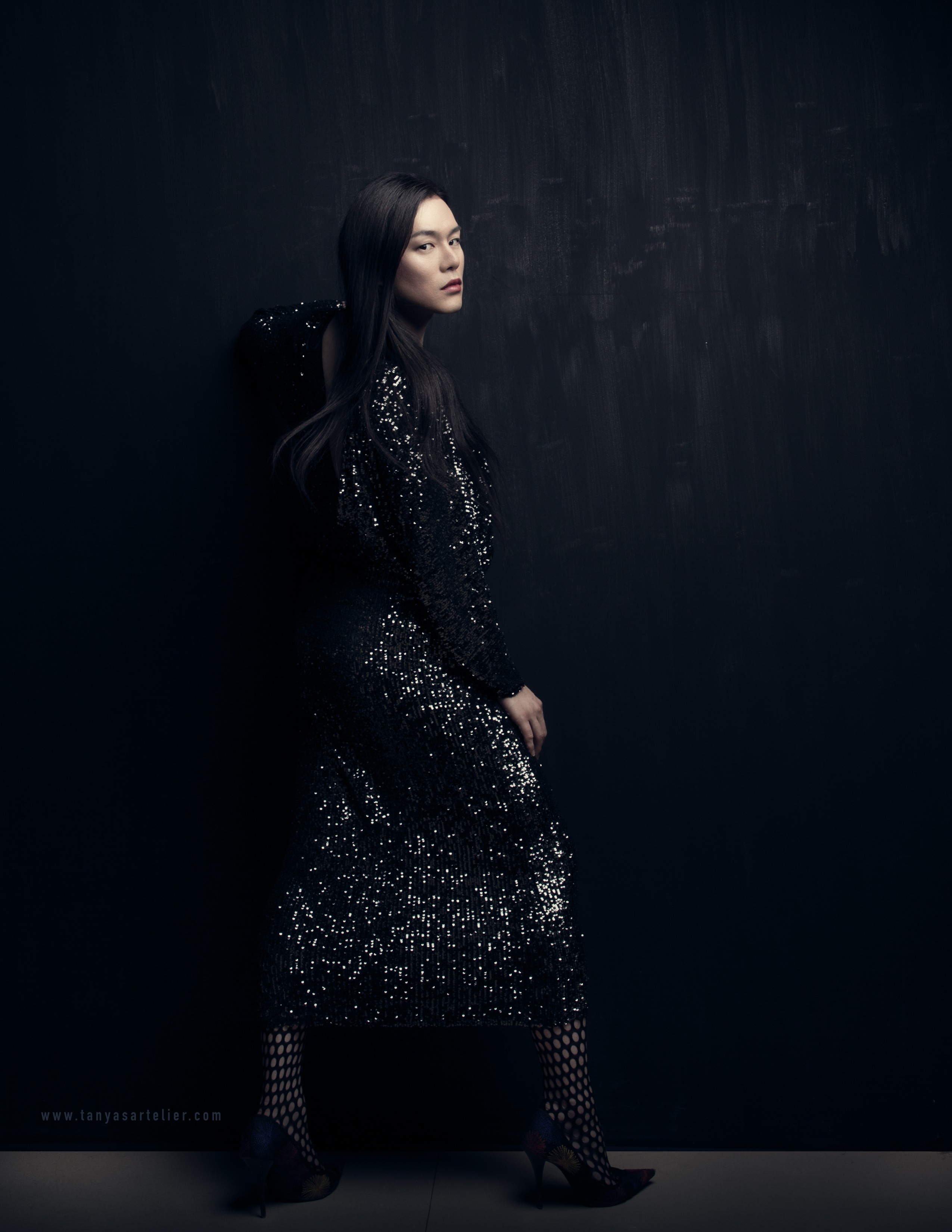 A woman in a black sparkly dress and long black hair looking over their shoulder at the camera