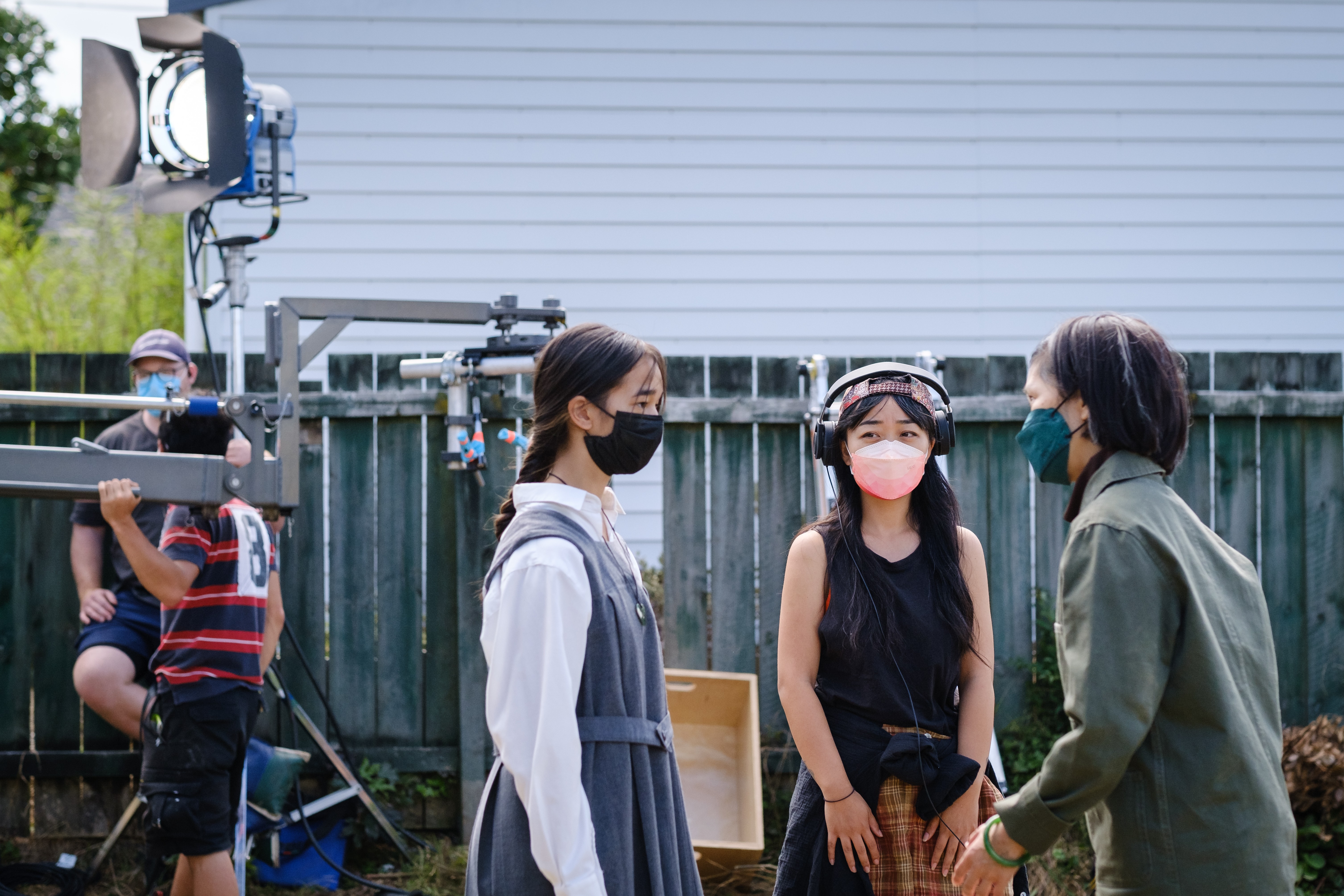 Three people standing outdoors on a film set in masks