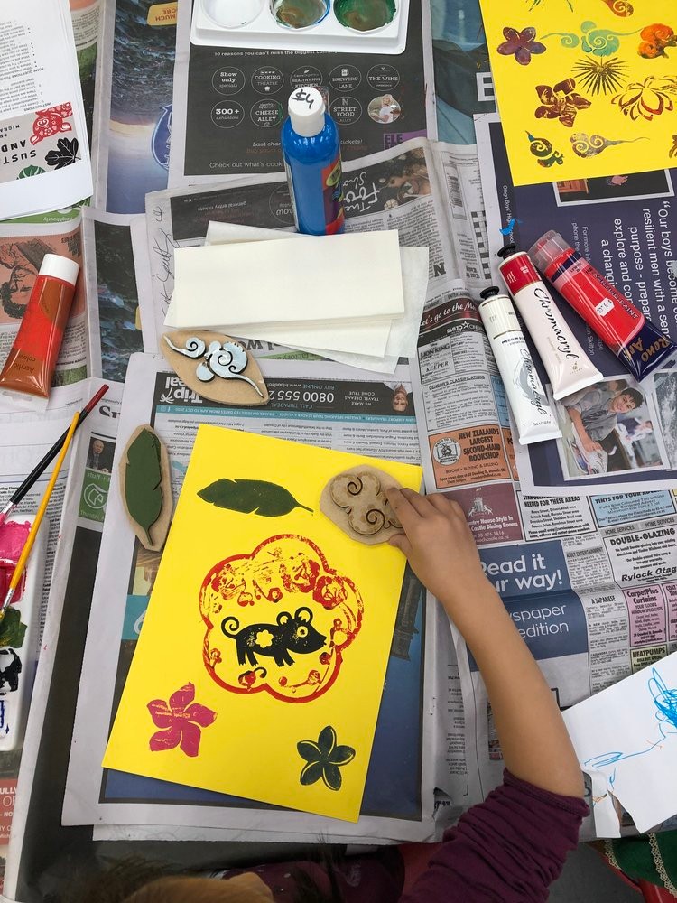 A hand stamping ink onto yellow card with various arts and crafts supplies in the background