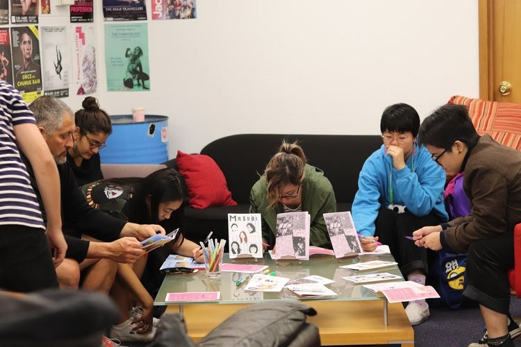 A group of people sitting together and concentrating on making zines. 