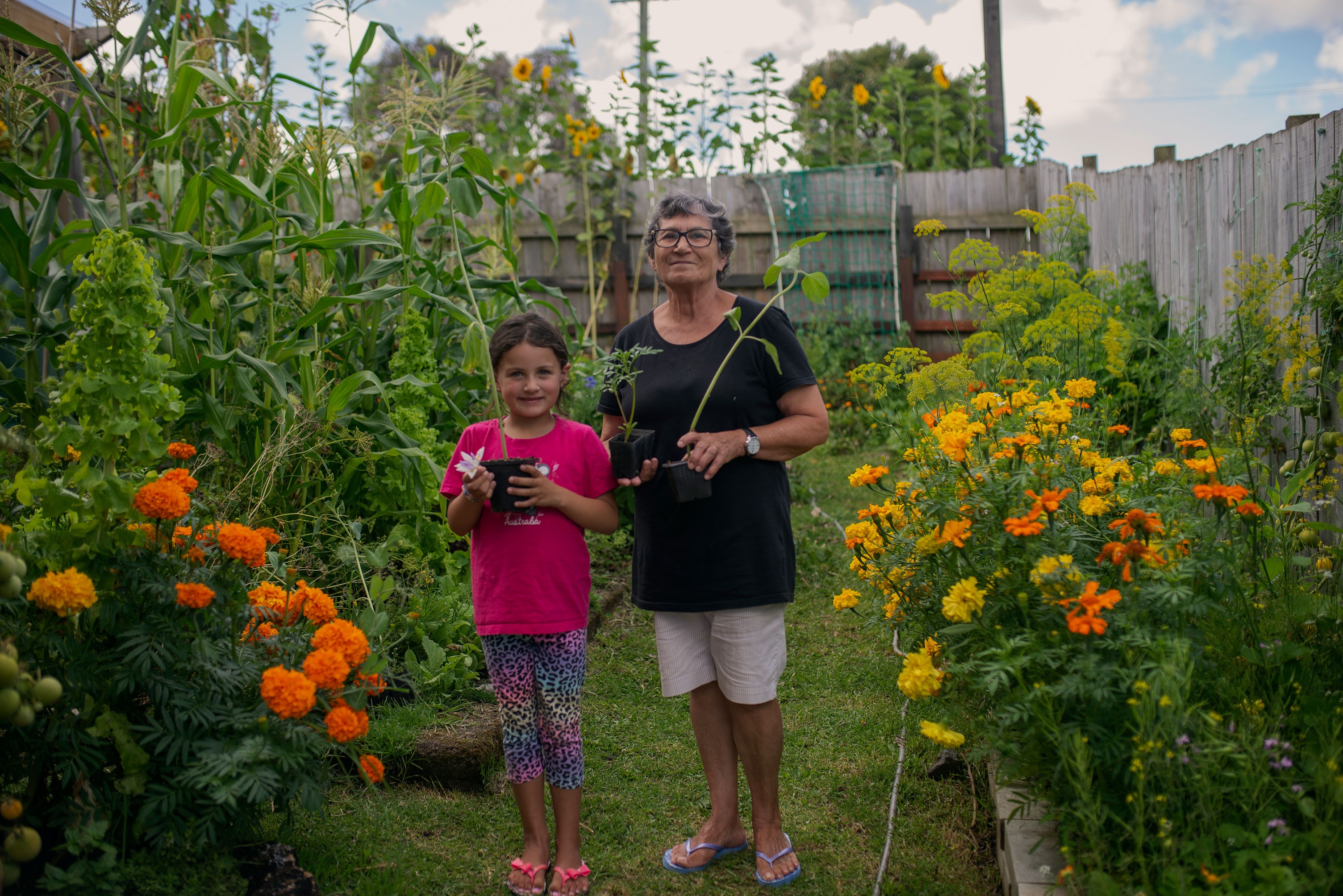 A young kid with her nana holding up seedlings in front of a lush garden