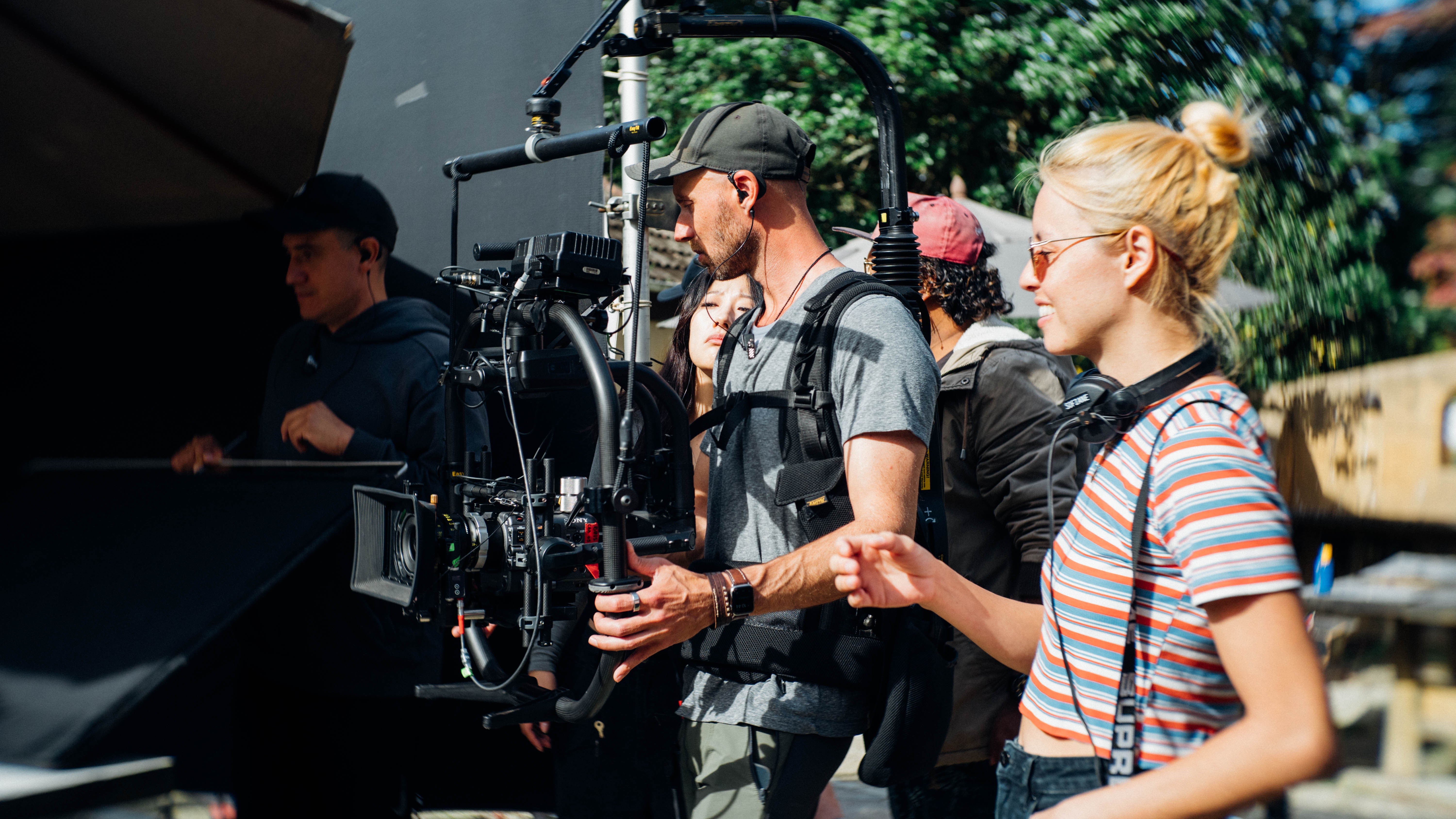 A woman with bleached hair and a striped top stands behind a camera.