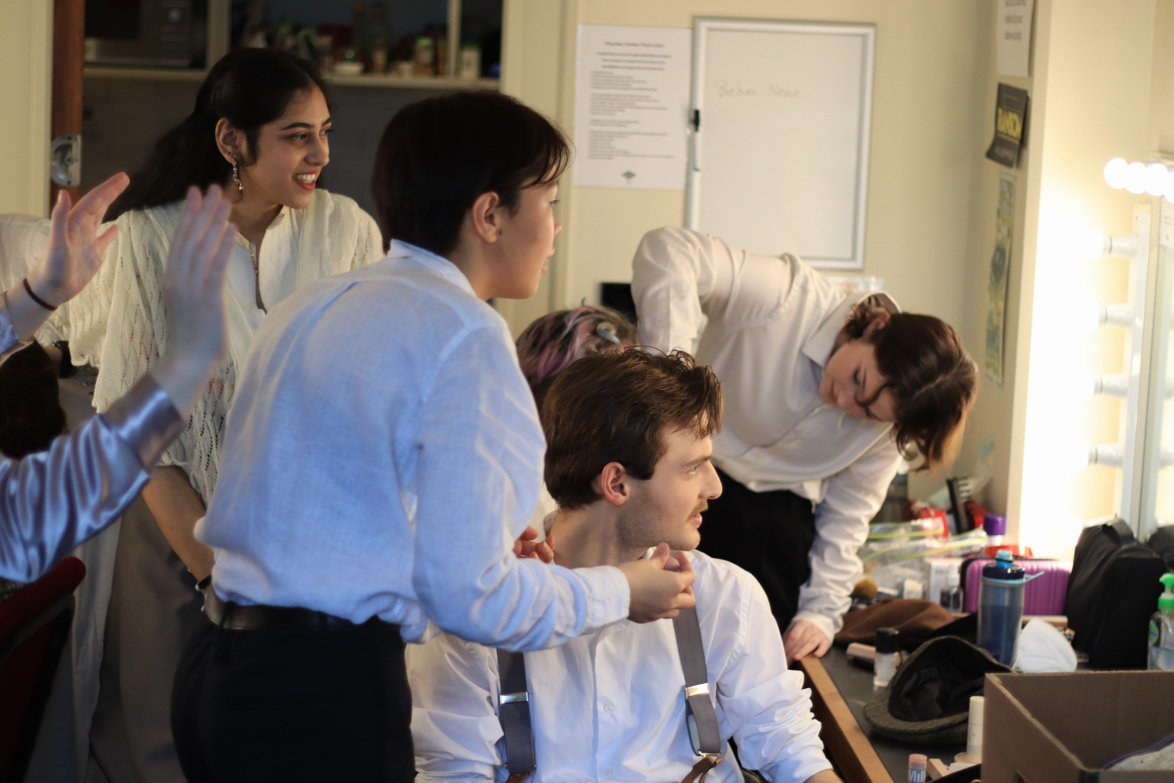 Five students backstage getting ready. Two students help two other students with make-up