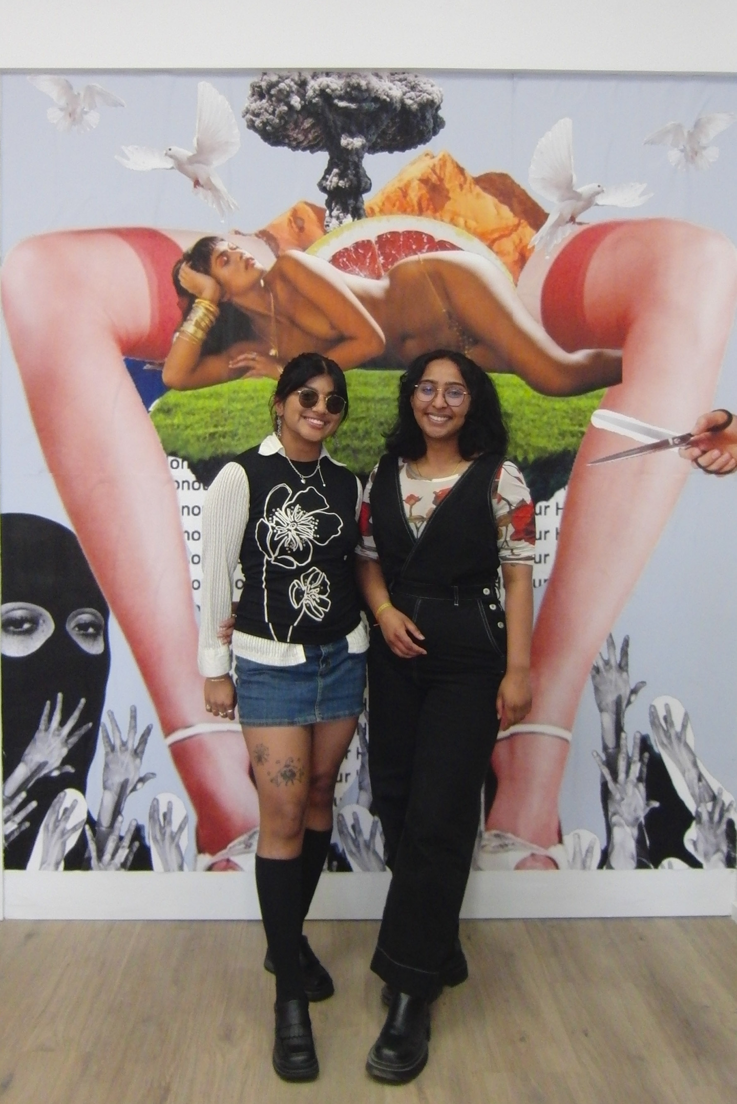 Two people smiling and standing in front of a collaged artwork. 