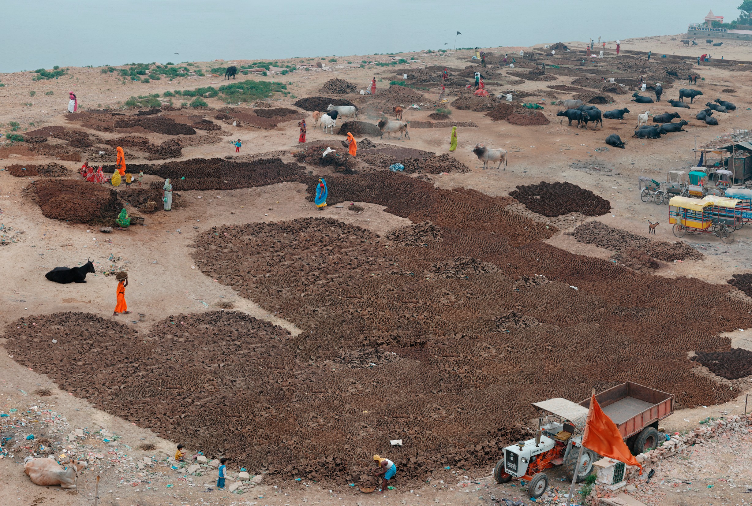 A large expanse of land near a river is worked by people in bright blue and orange clothing.