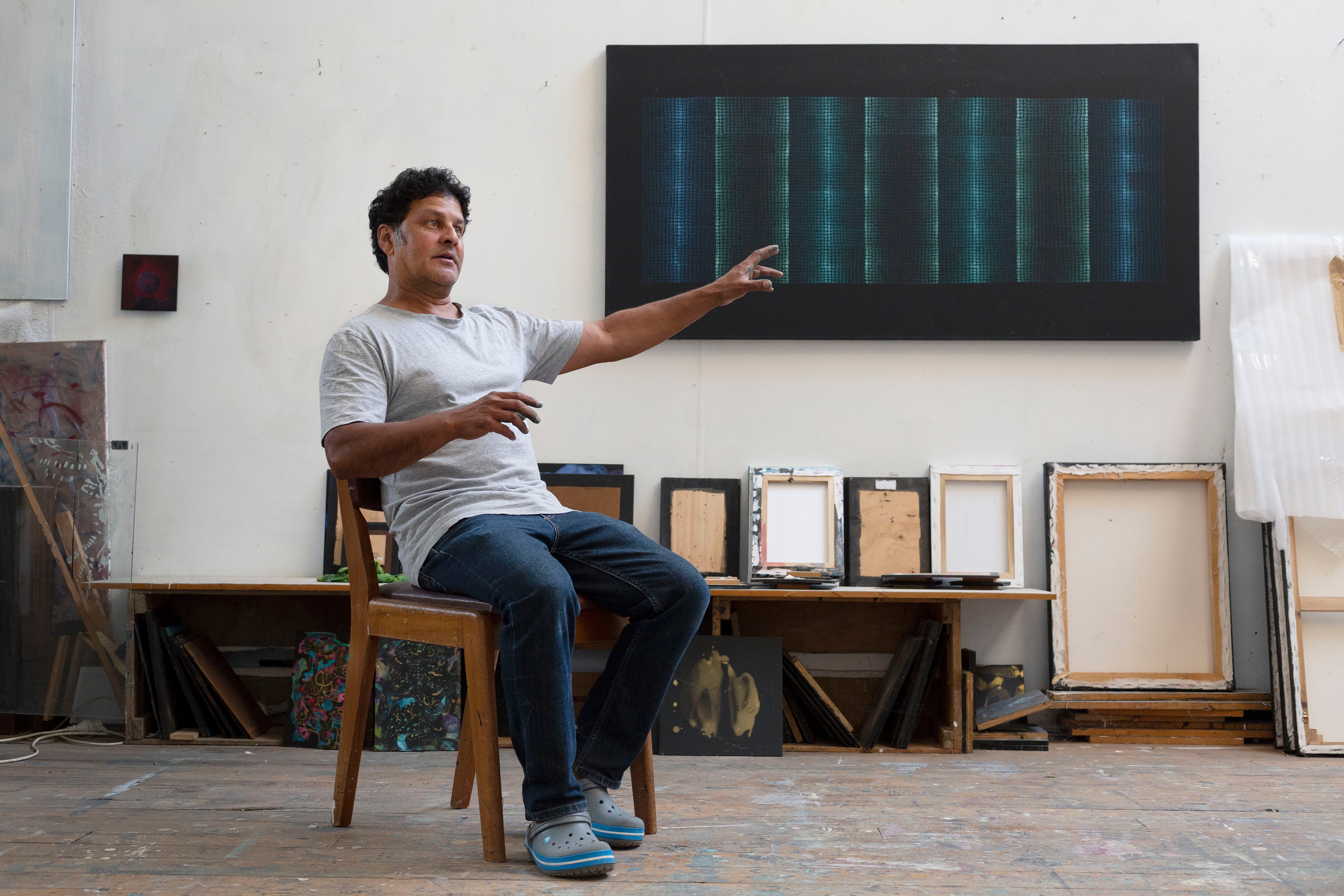 A person sitting on a chair in front of a wall of paintings