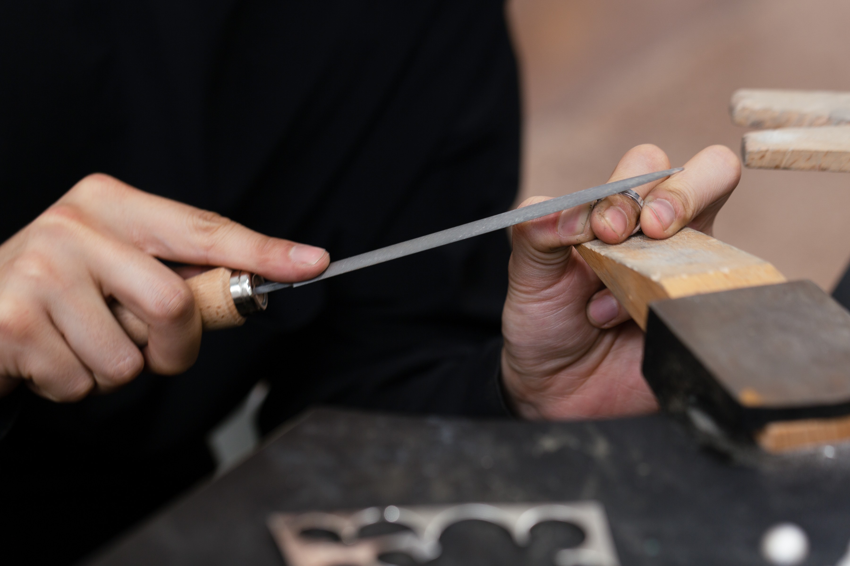 Close-up on hands filing a silver ring against a wooden stand