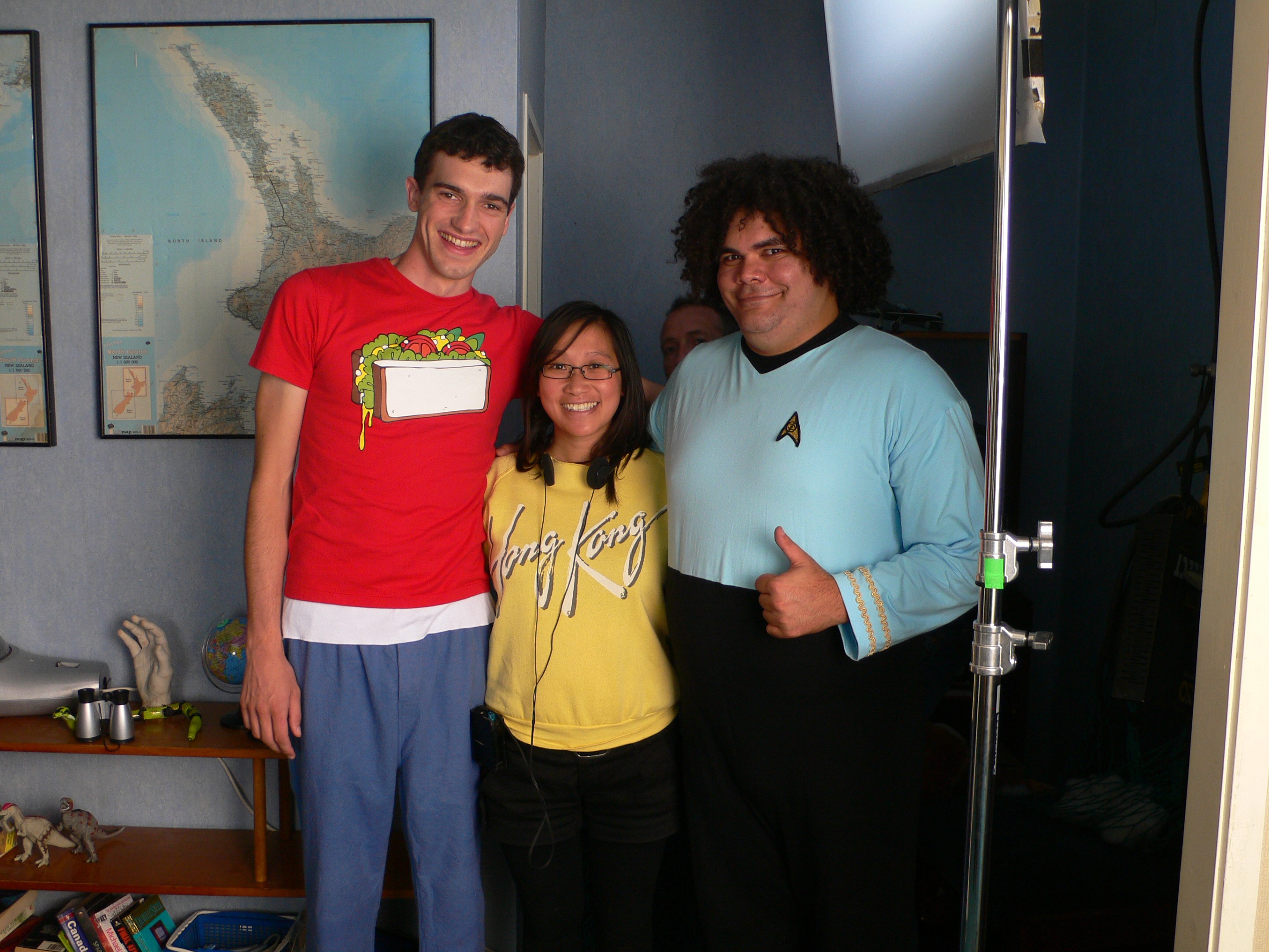 A Chinese woman with a yellow sweater with 'Hong Kong' on it stands between two male actors