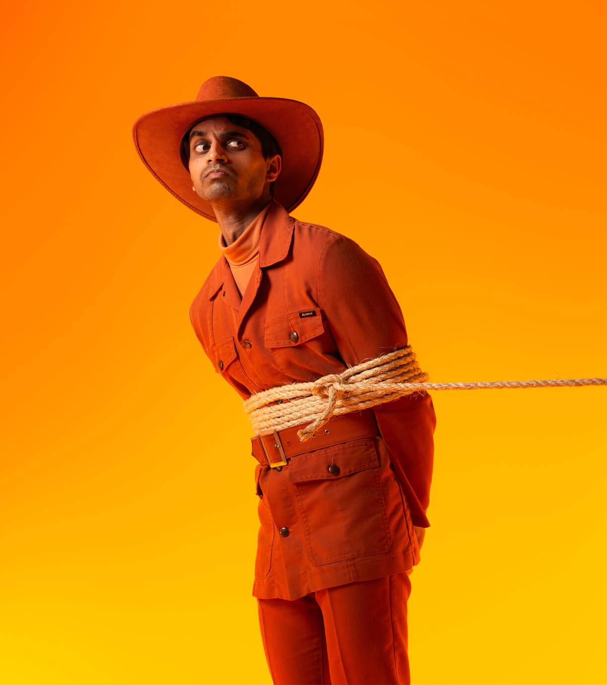 A man in an orange cowboy suit is held by a lasso