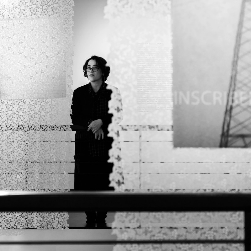 A black and white image of a woman in a dark coat standing behind an installation