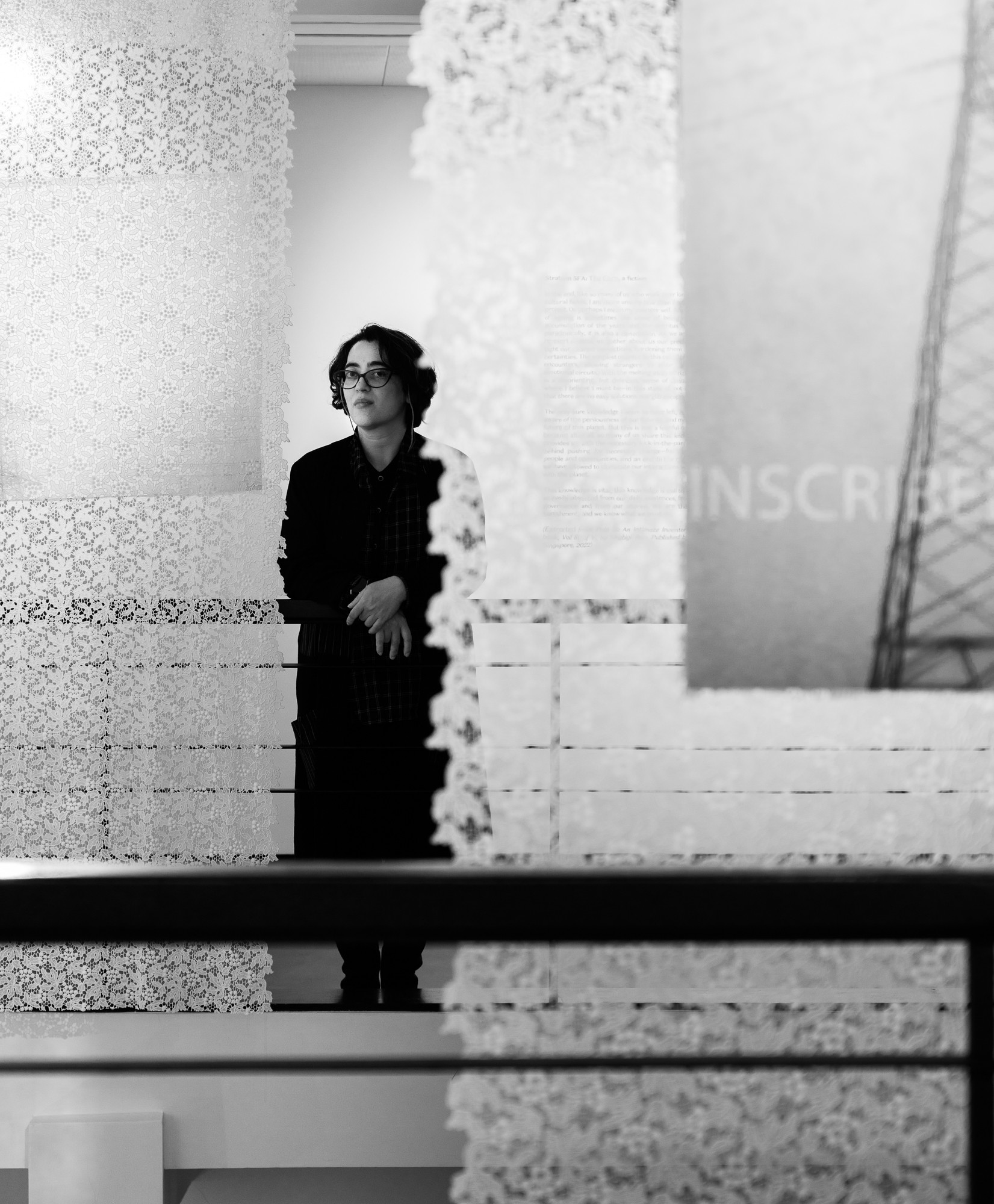 A black and white image of a woman in a dark coat standing behind an installation