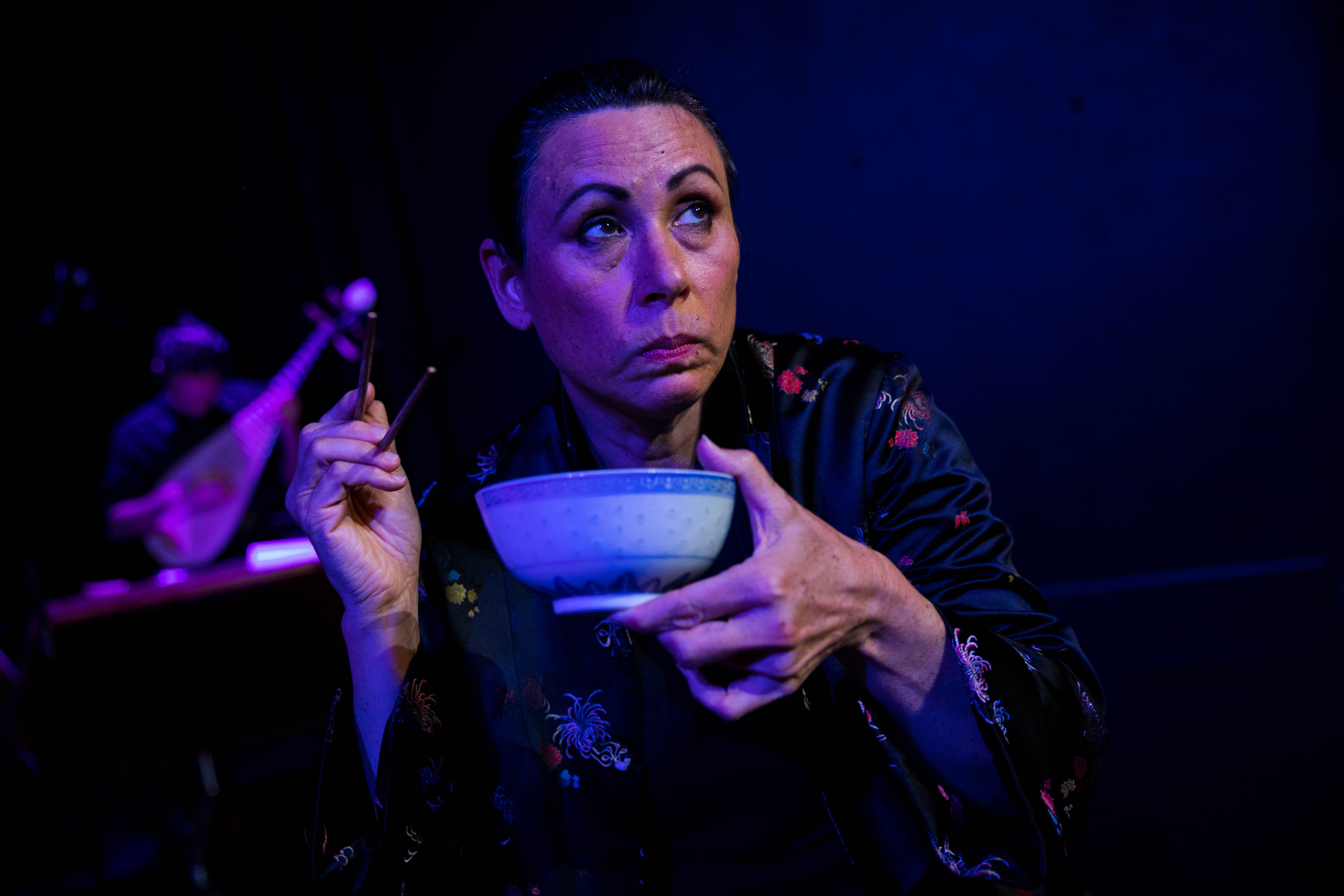 Lynda Chanwai Earle on stage holding a Chinese bowl and chopsticks.