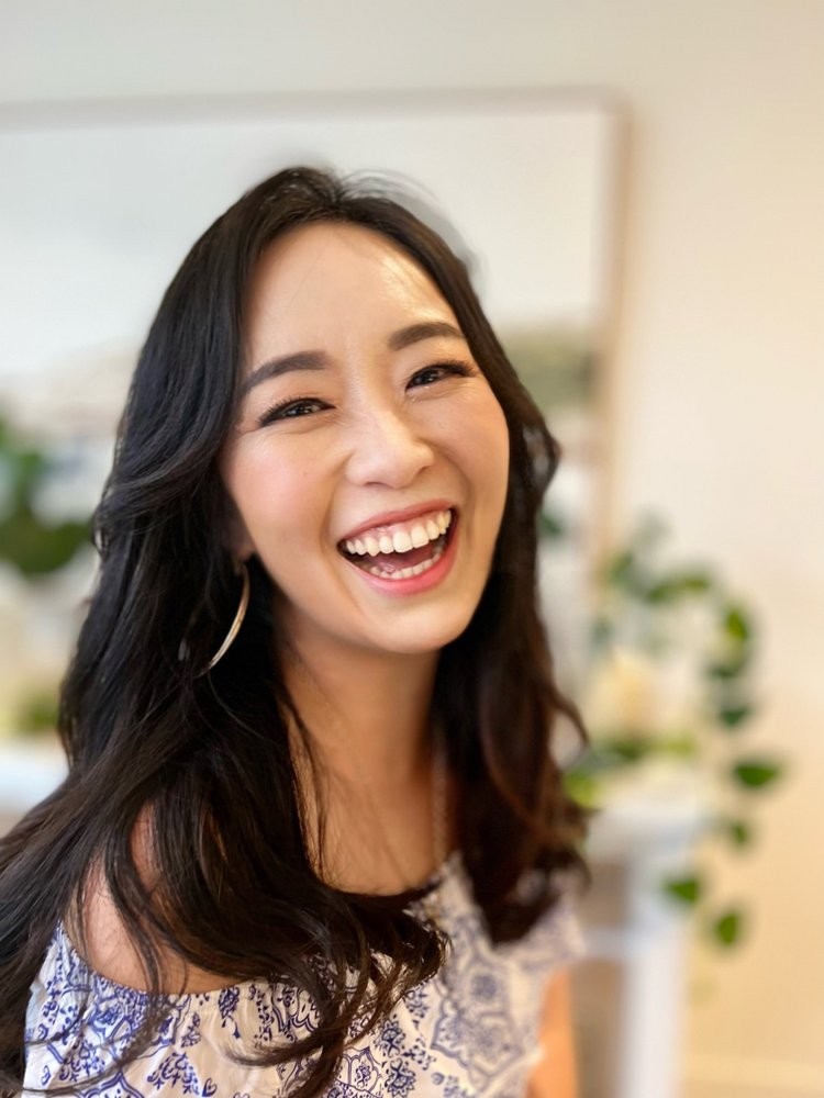 A close-up of a woman with long wavy black hair laughing at the camera