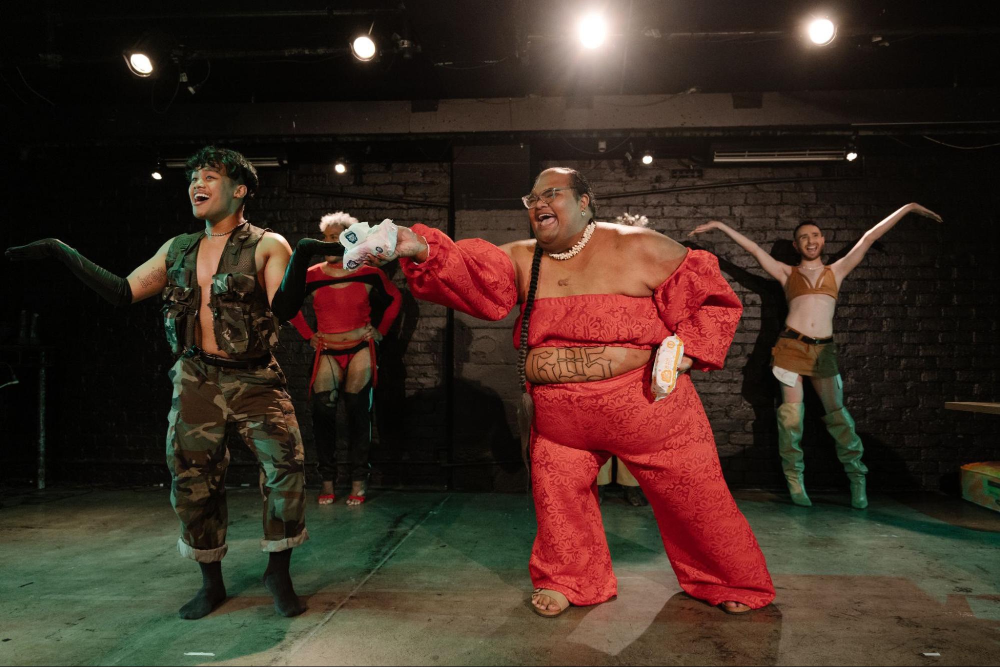 Action photo of a dance performance with smiling eclectic performers wearing fashionable body-revealing outfits