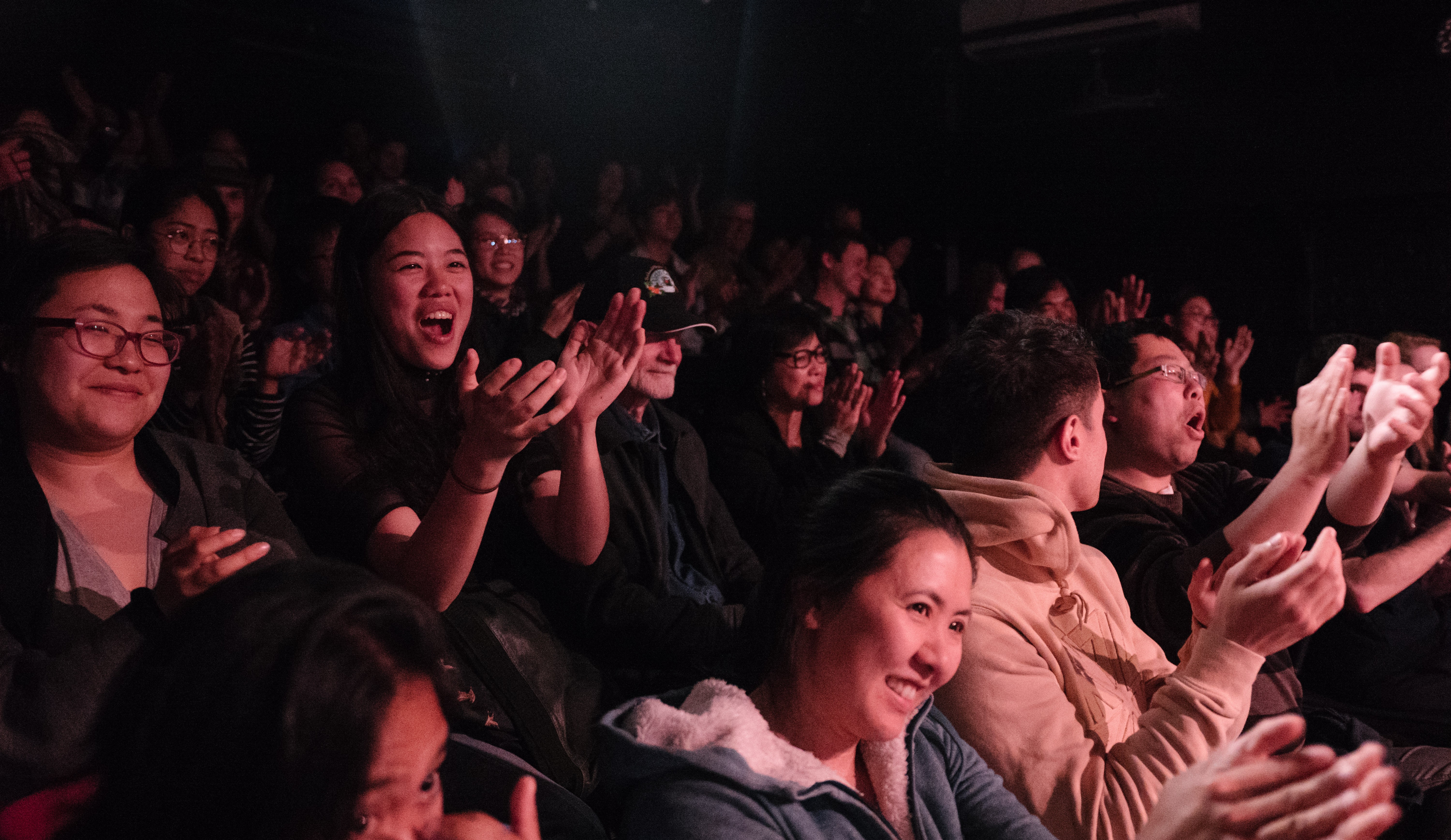 An audience lit by pink light smiling and clapping