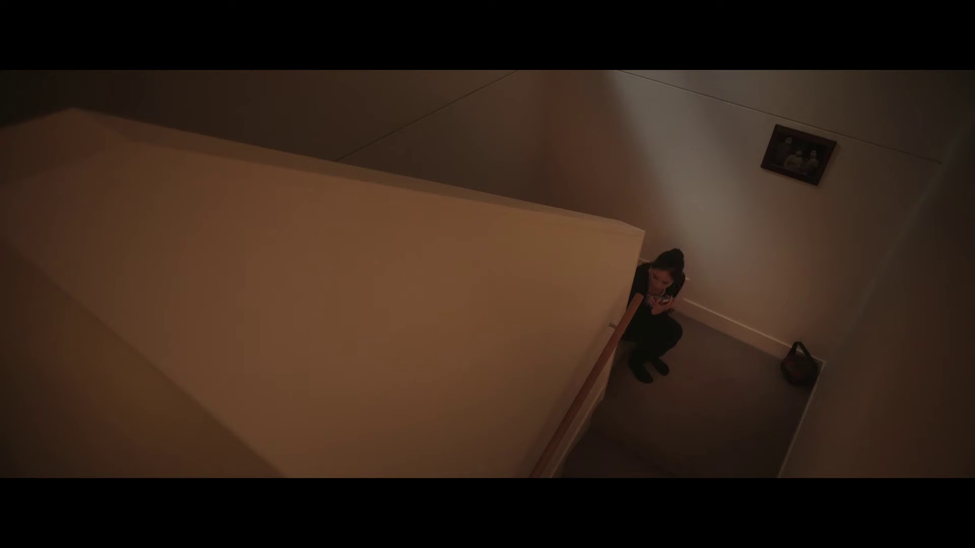 In a scene from the filmn "Munkie", a woman is crouched on a flight of stairs with a cellphone in her hand. 