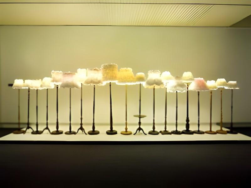 A row of illuminated lanterns with shades covered in white fabric and plastic hibiscus flowers.