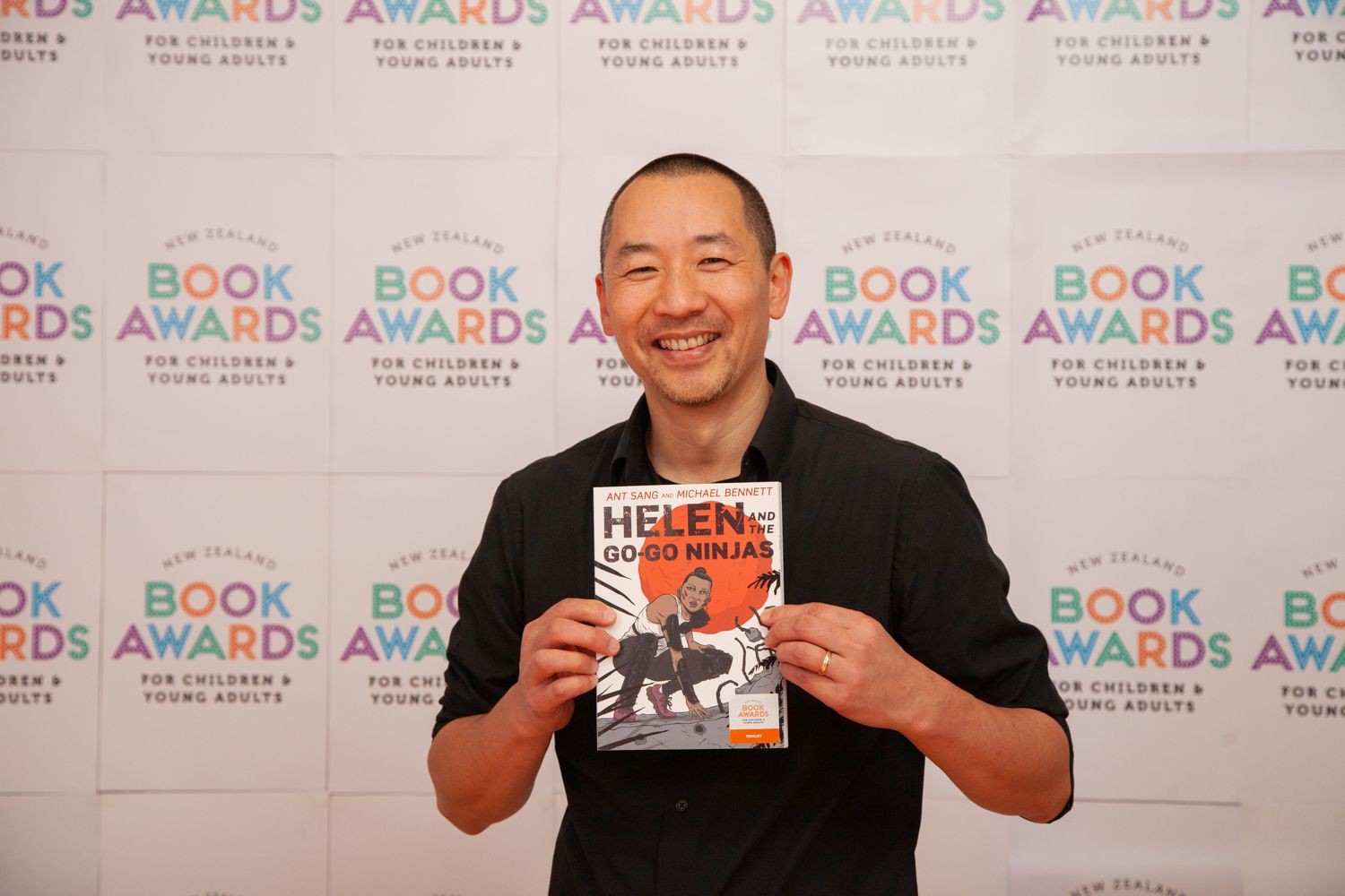 A man holding a book in front of an awards backdrop. 