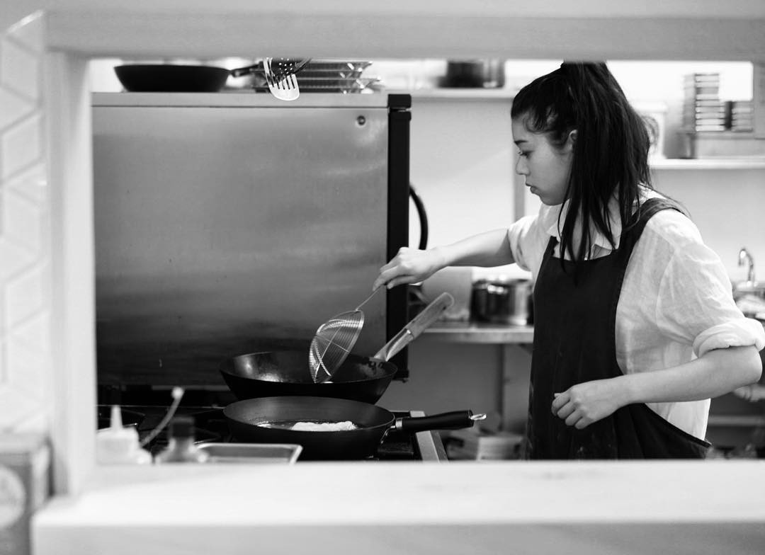 Black and white photo of a woman standing at a stove