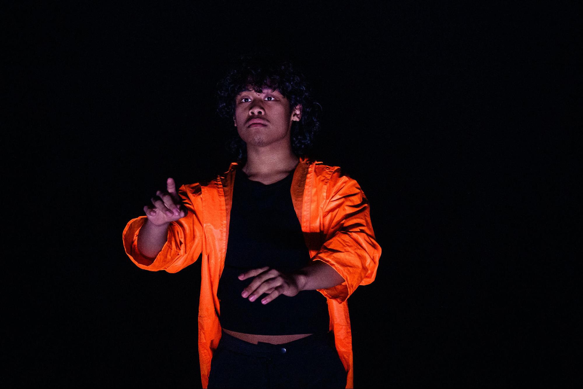 Dramatic image of Filipino-looking person in fluorescent orange jacket emerging from a black background