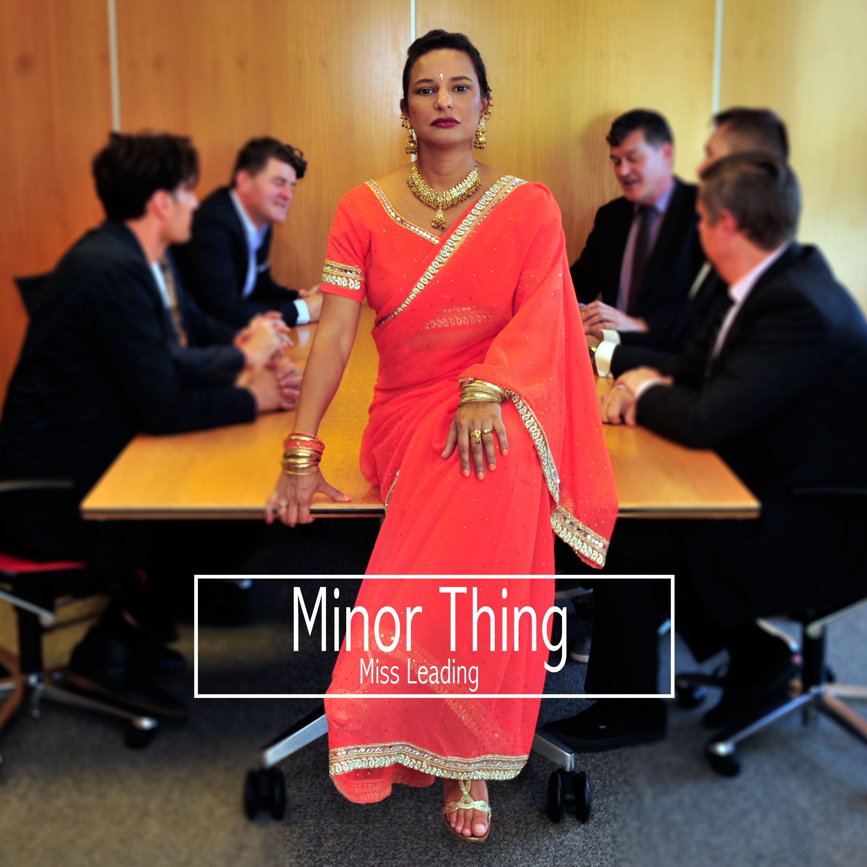 A person in an orange sari sitting on an office table with men in suits sitting around it. 