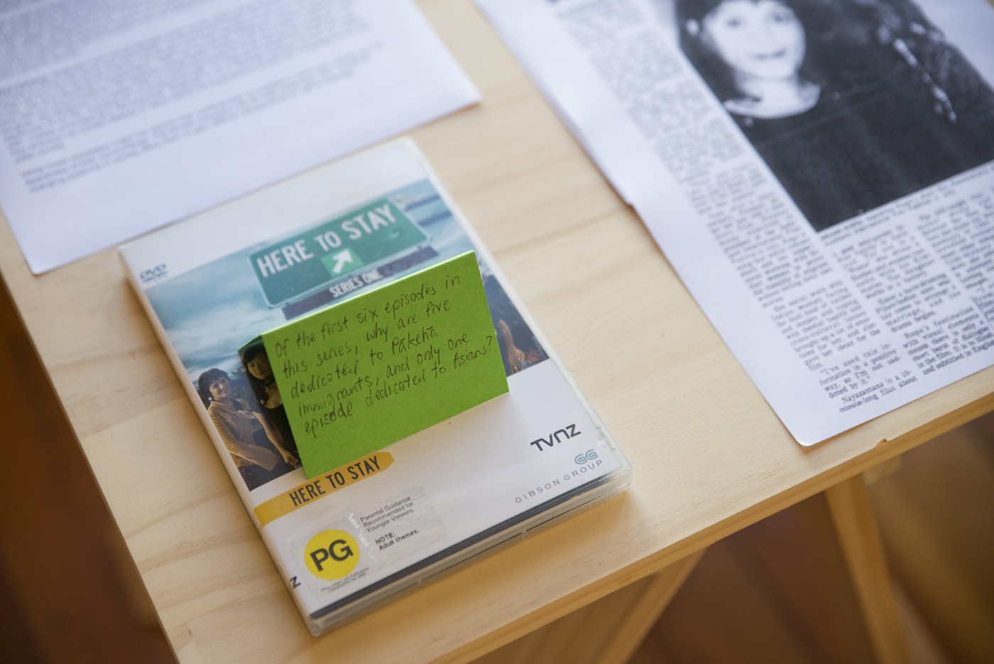 A DVD called 'Here to Stay' next to printed articles on a trestle table.