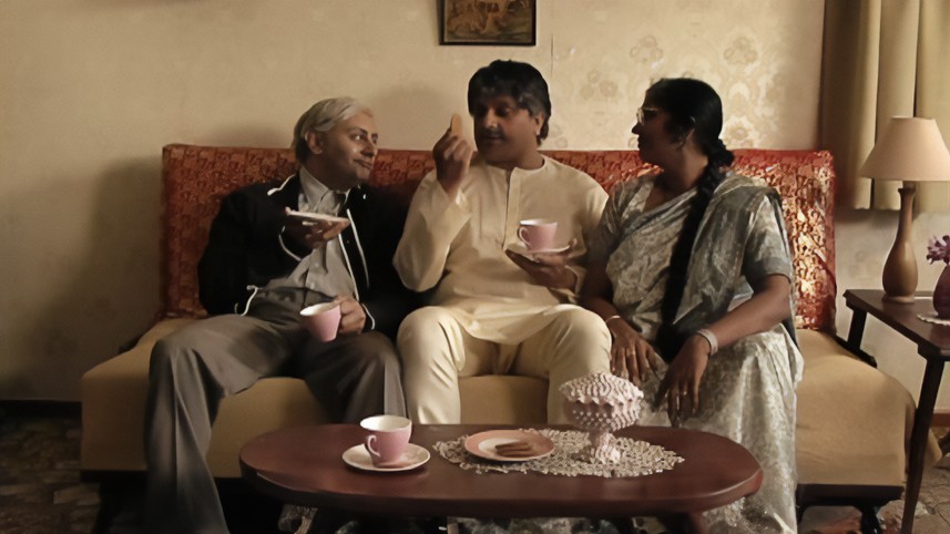 In a scene from ‘A Thousand Apologies’, two men and a woman sit on a sofa, drinking tea.