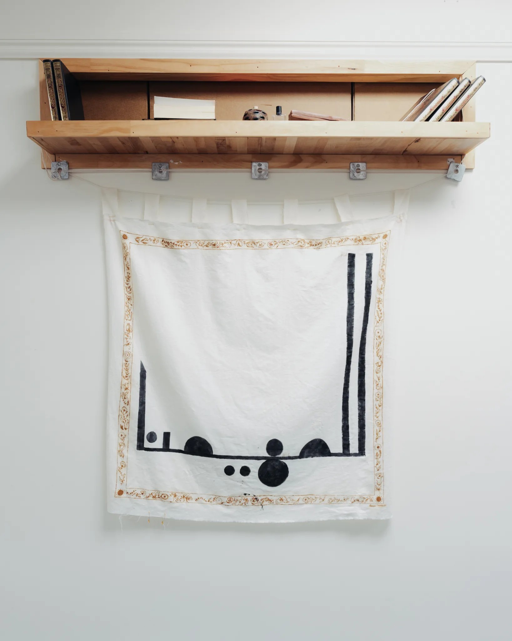 White fabric with a large black pattern and detailed henna border hangs from a wall.