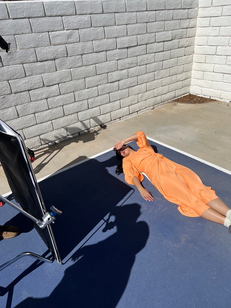 A woman in an orange dress lies on a blue mat surrounded by a white brick wall