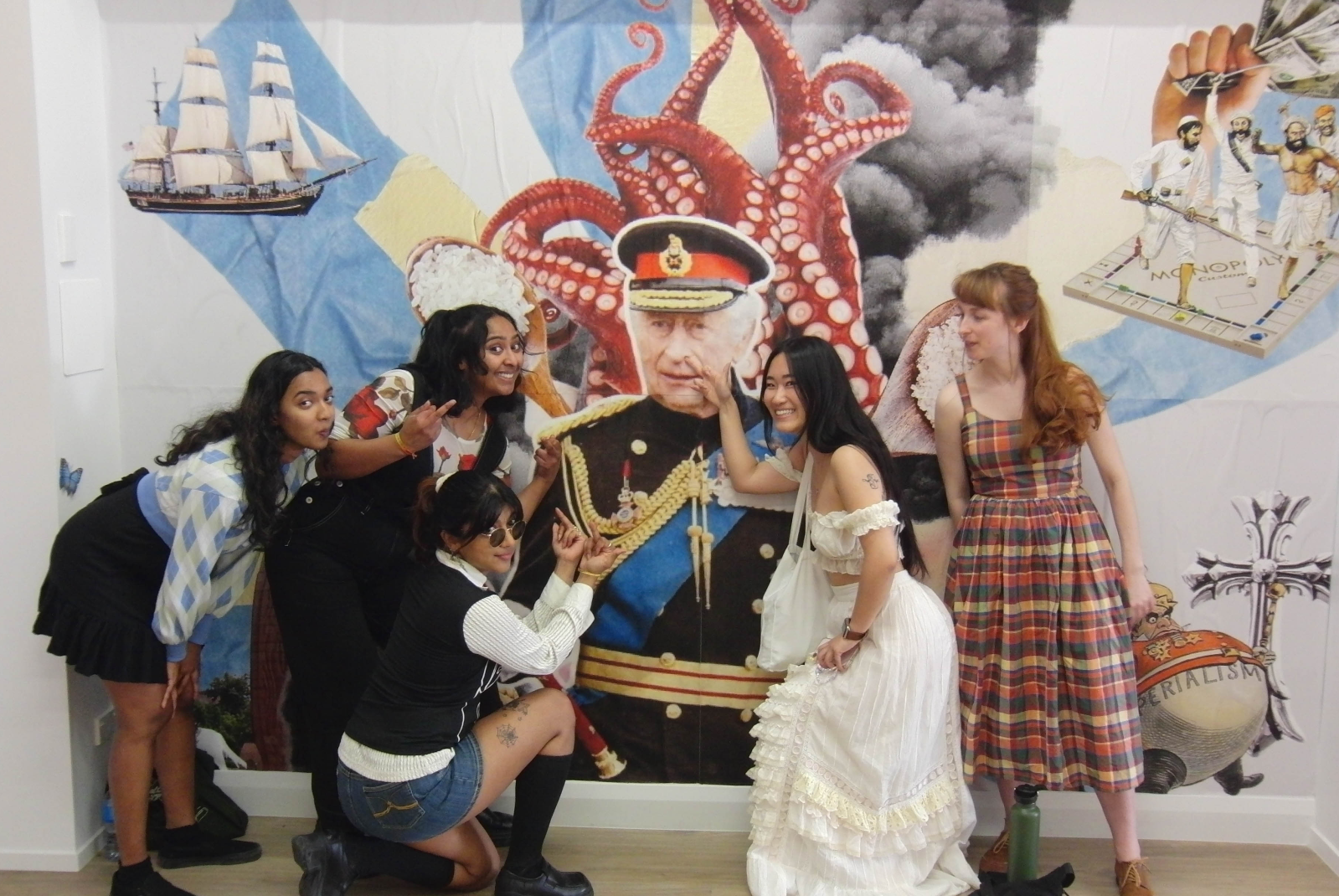 A group of people smiling in front of a collage of King Charles and pulling the finger. 