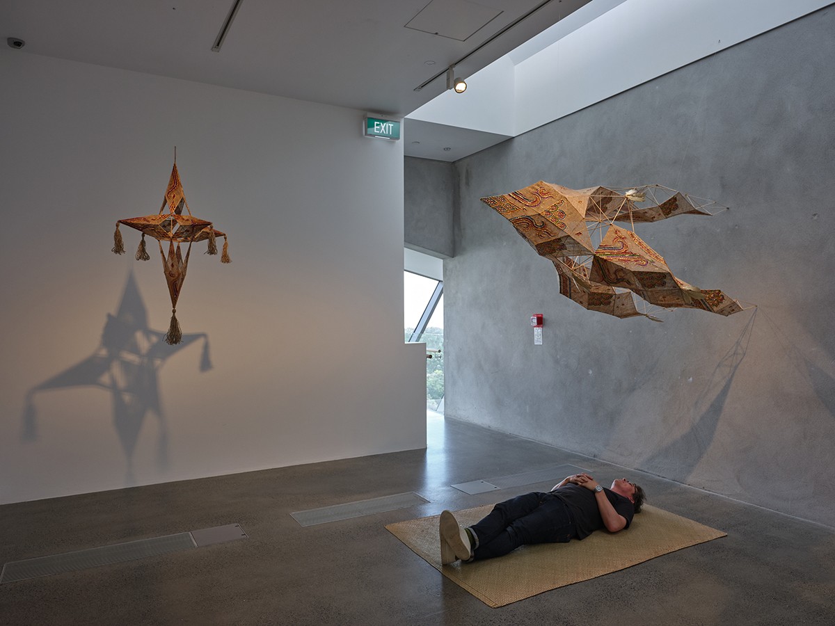 A person is lying on a woven mat looking up at two suspended scultpures of stylised stars