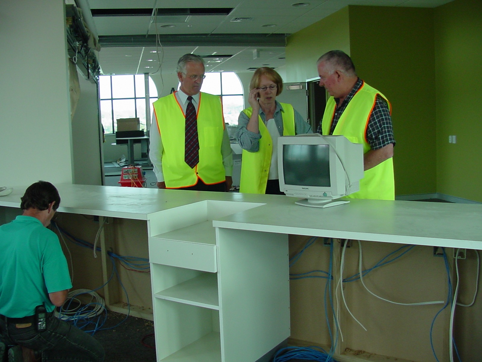 Three people in fluoro vests look over a computer terminal in a library under construction