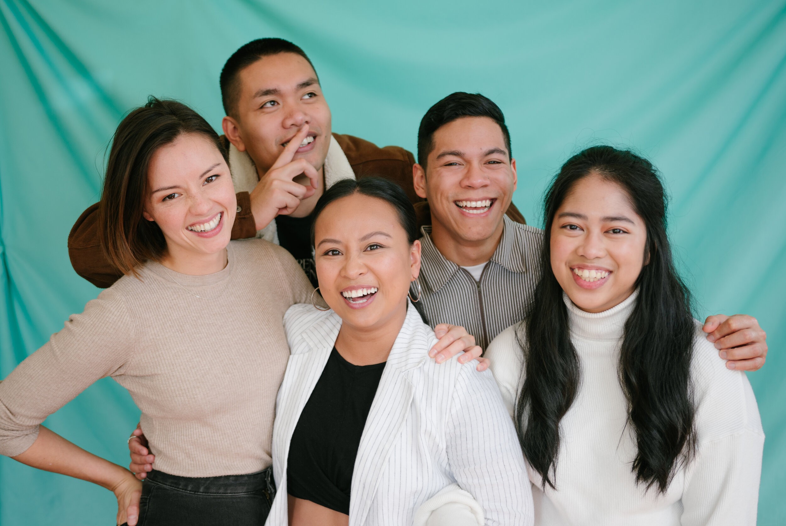 Five people of Asian descent smiling in front of a green background